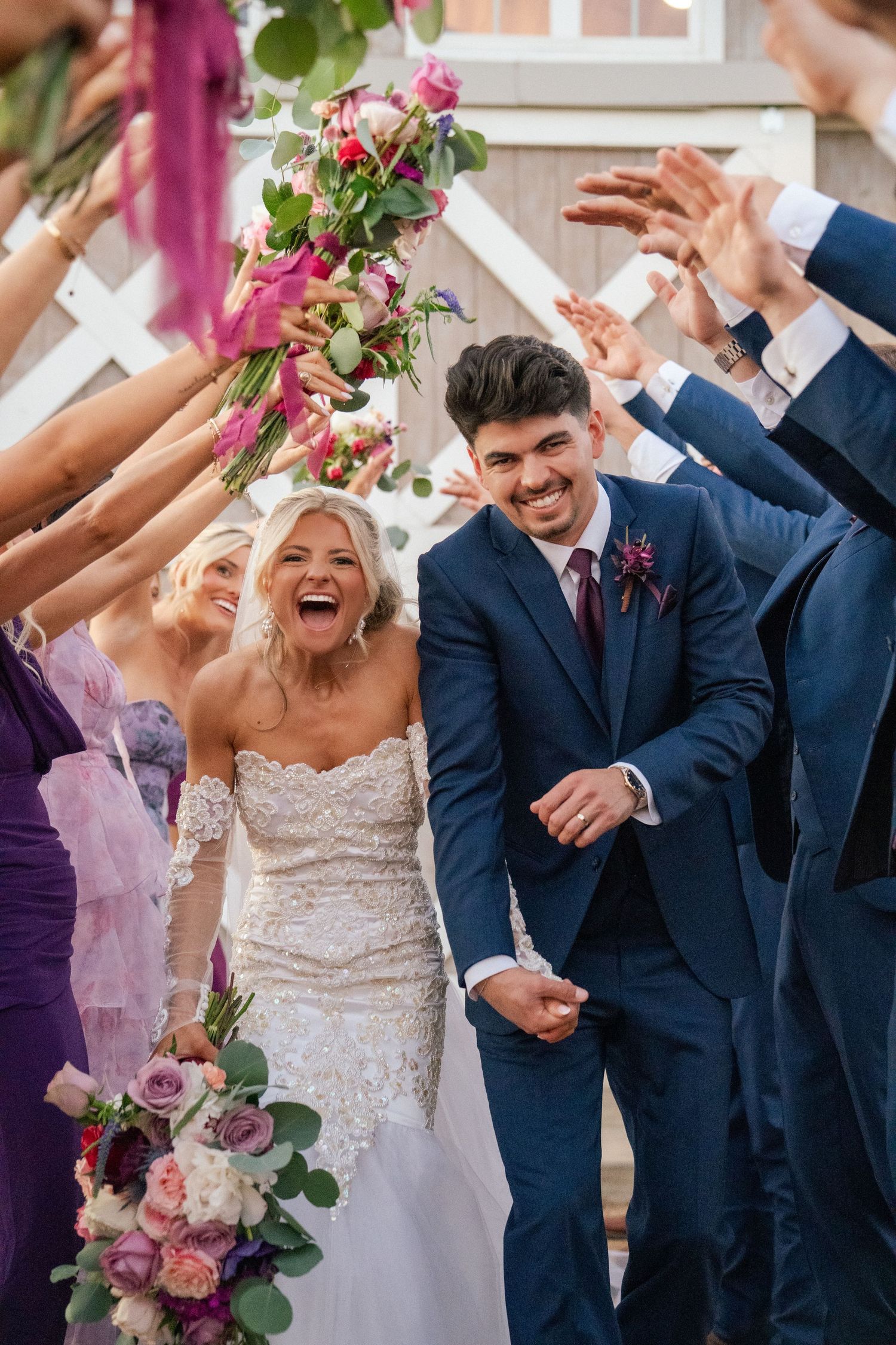 Joyful bride and groom walk through cheering guests after outdoor wedding ceremony.