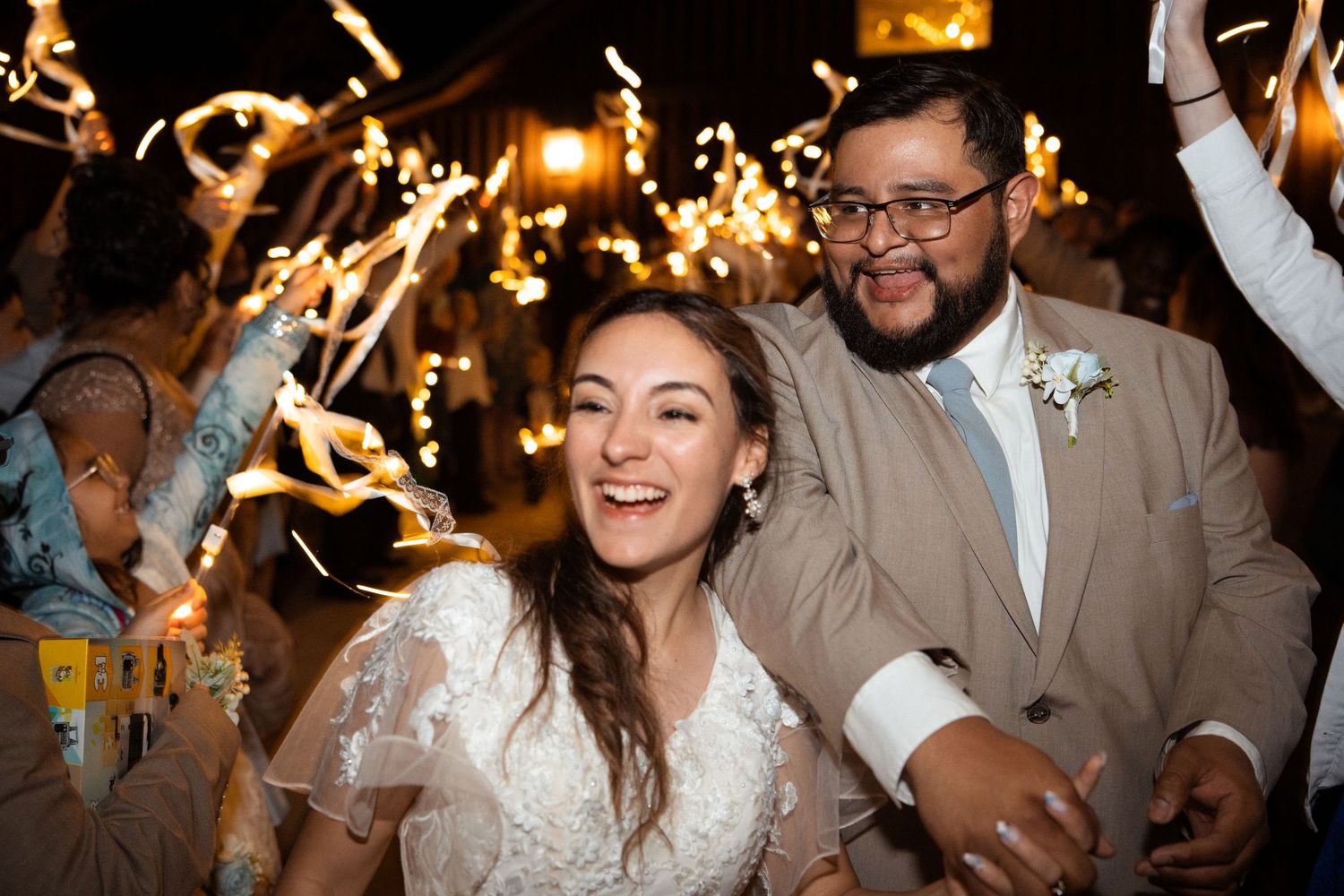 Joyful bride and groom celebrating their sparkler exit at a festive evening wedding reception.