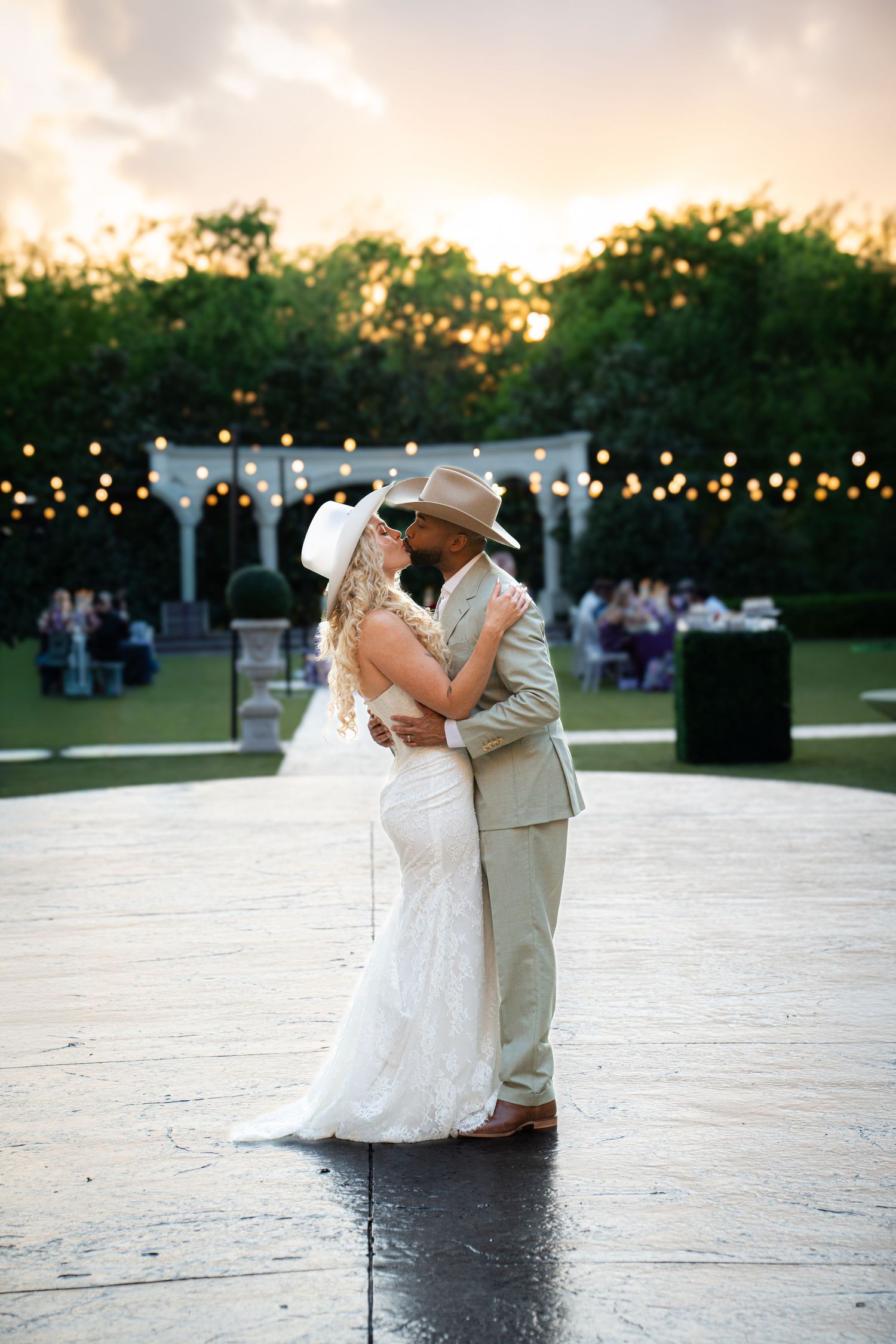 Bride and groom in cowboy hats sharing first dance on outdoor dance floor at sunset.