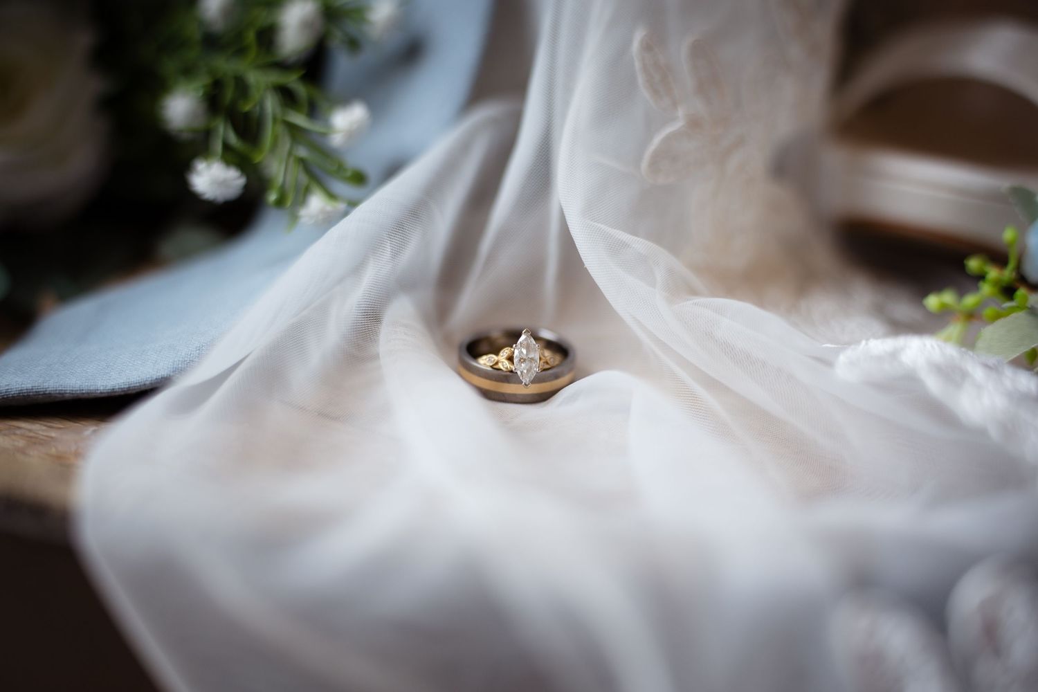 Close-up of a gold diamond engagement ring resting in a small dish on a white bridal veil.