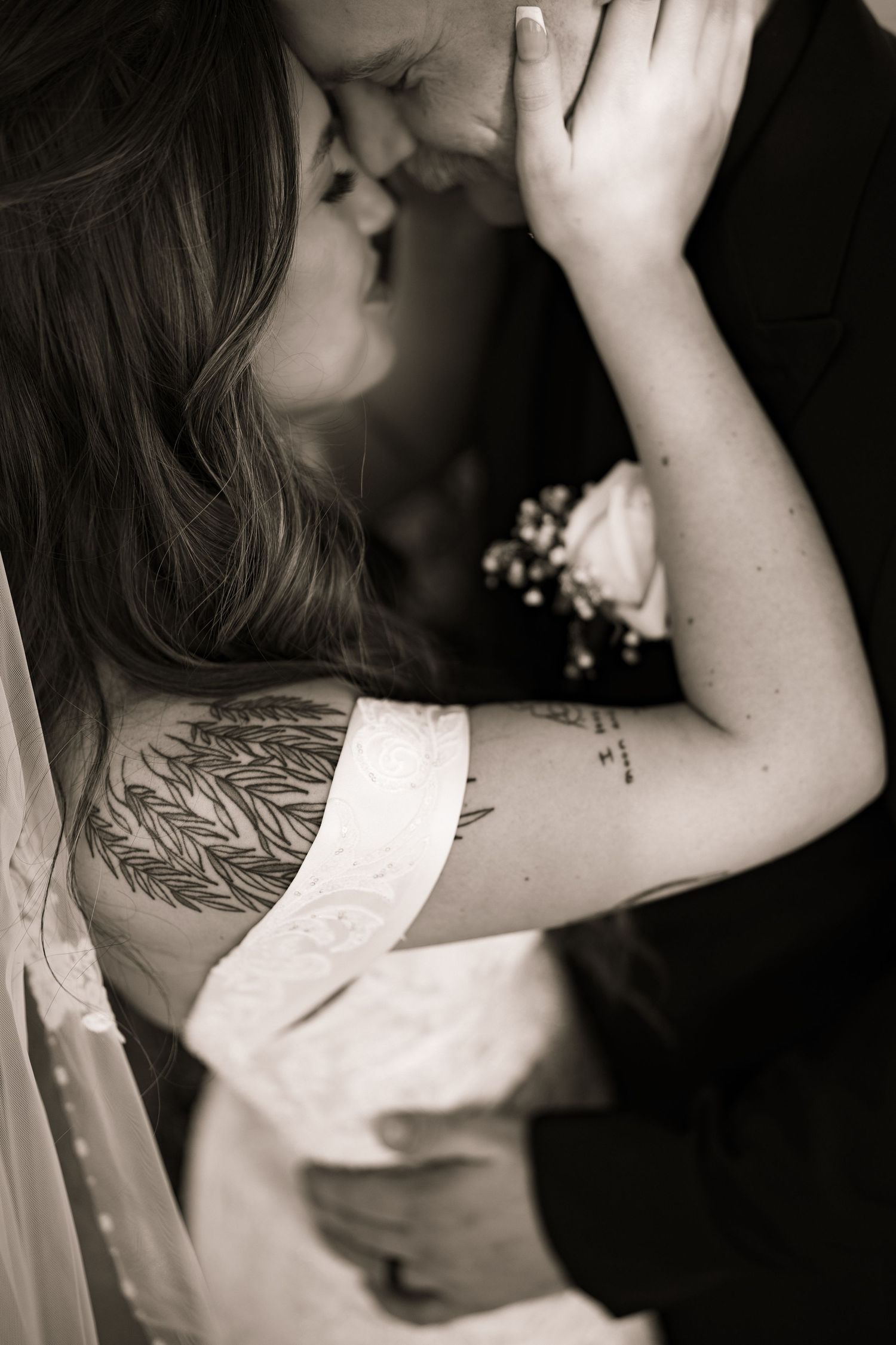 Black and white close-up of tattooed bride and groom sharing an intimate moment.