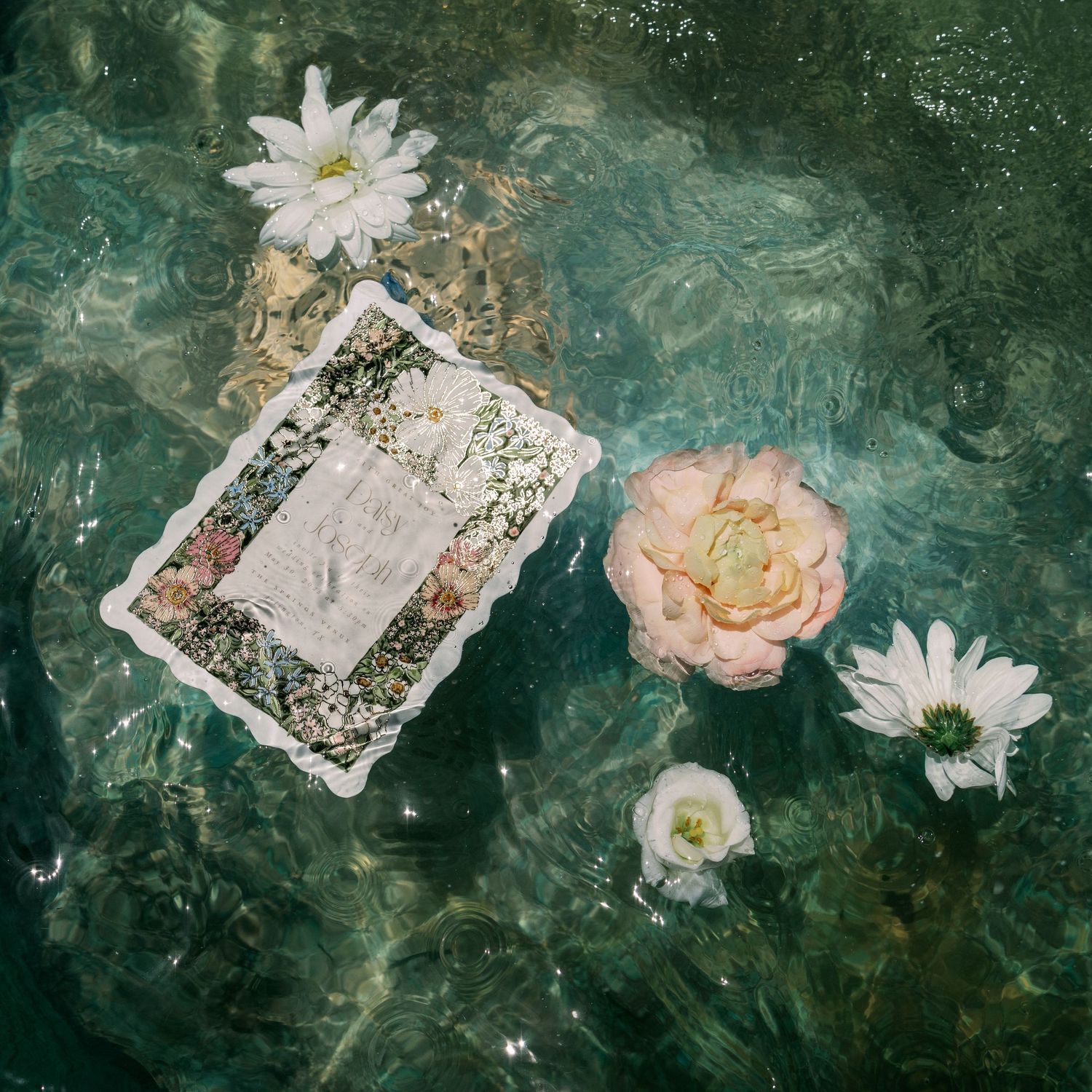 Aerial view of floating wedding invitation with flowers in clear turquoise water.