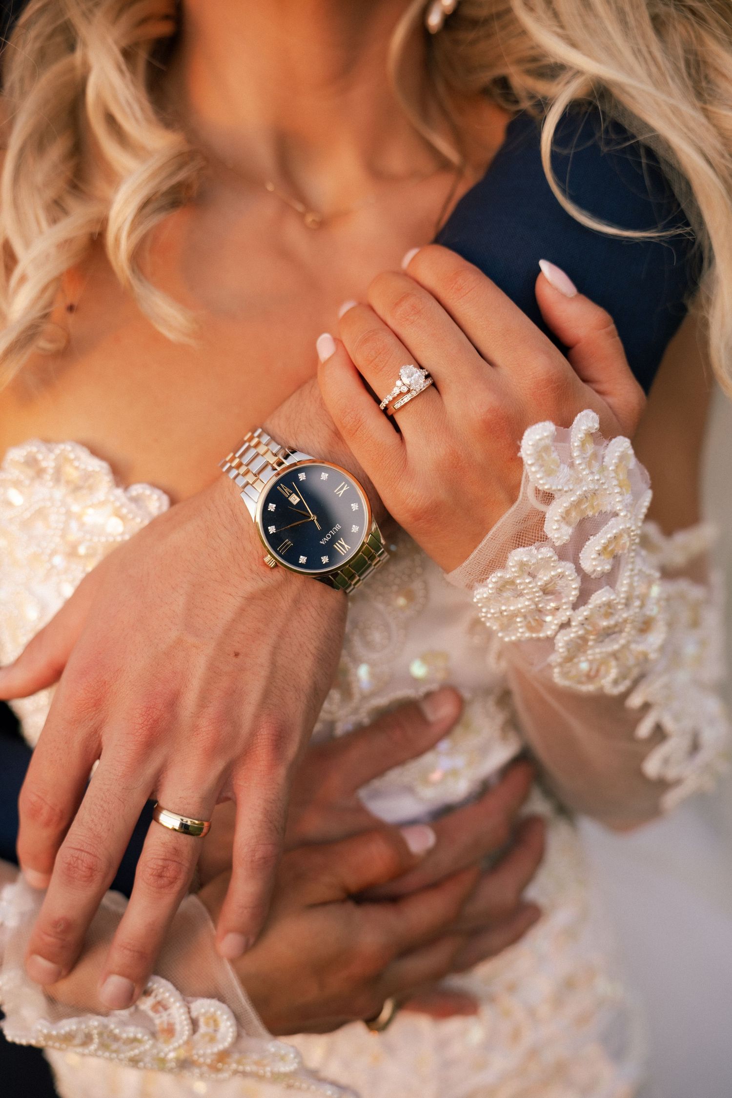 Close-up of bride and groom hands showing wedding rings, bride wearing elegant diamond ring and gold watch.