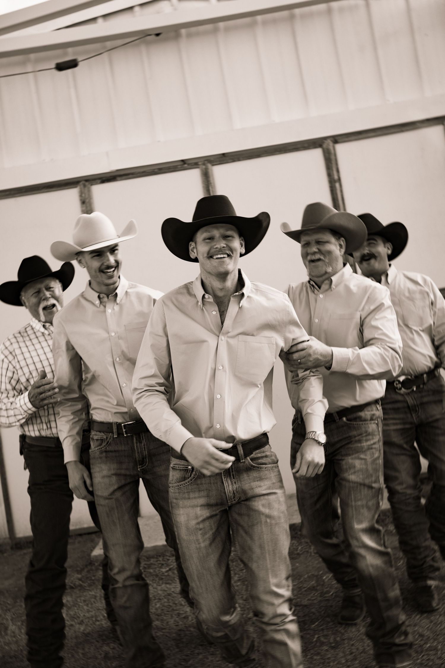 Group of smiling men in cowboy hats and jeans posing together at a western-style outdoor event.