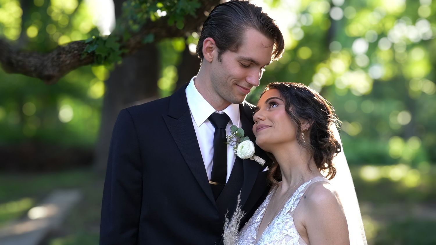 Happy bride and groom smile together outdoors surrounded by greenery on their wedding day.