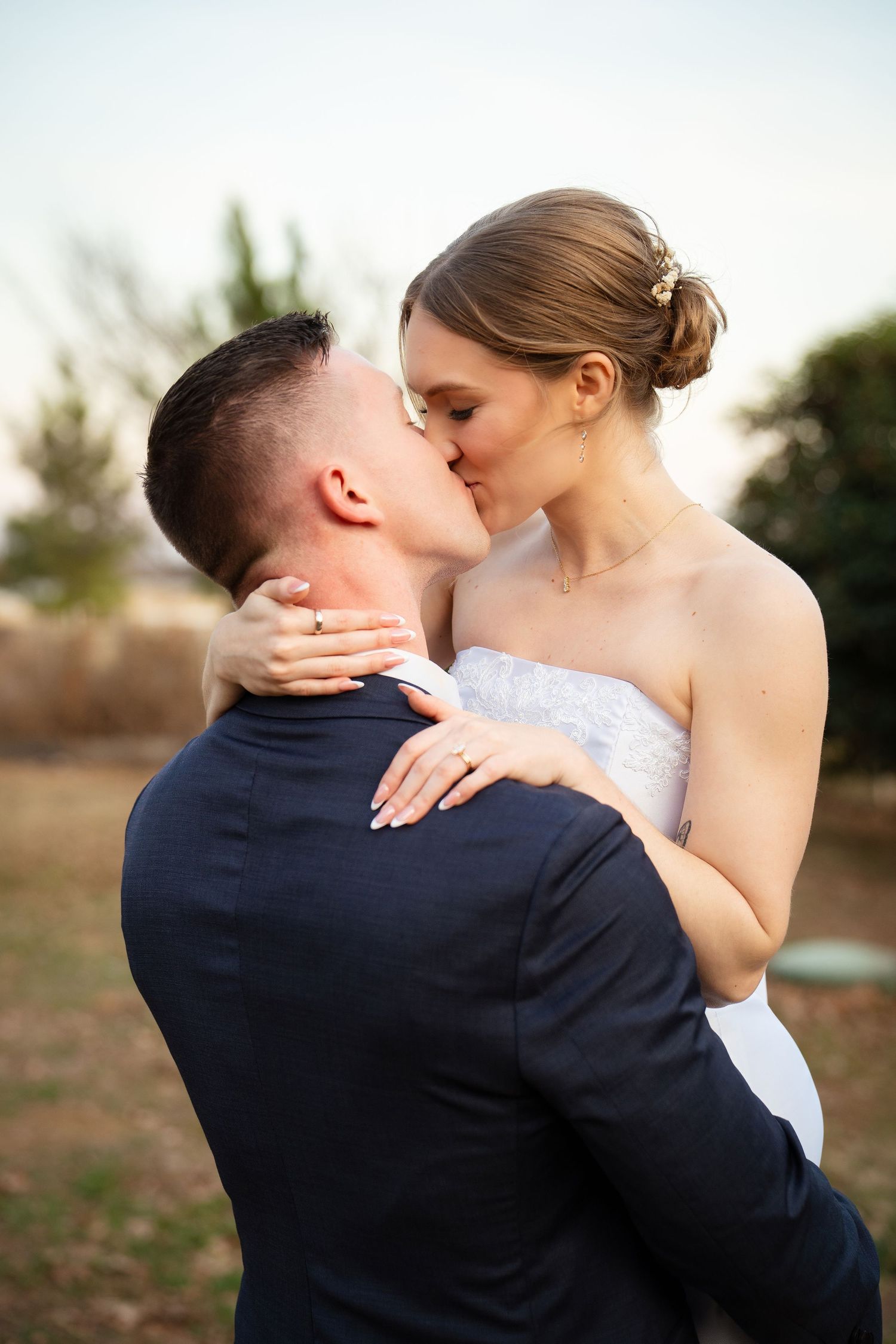 Bride and groom share a romantic kiss outdoors during golden hour wedding portrait session.