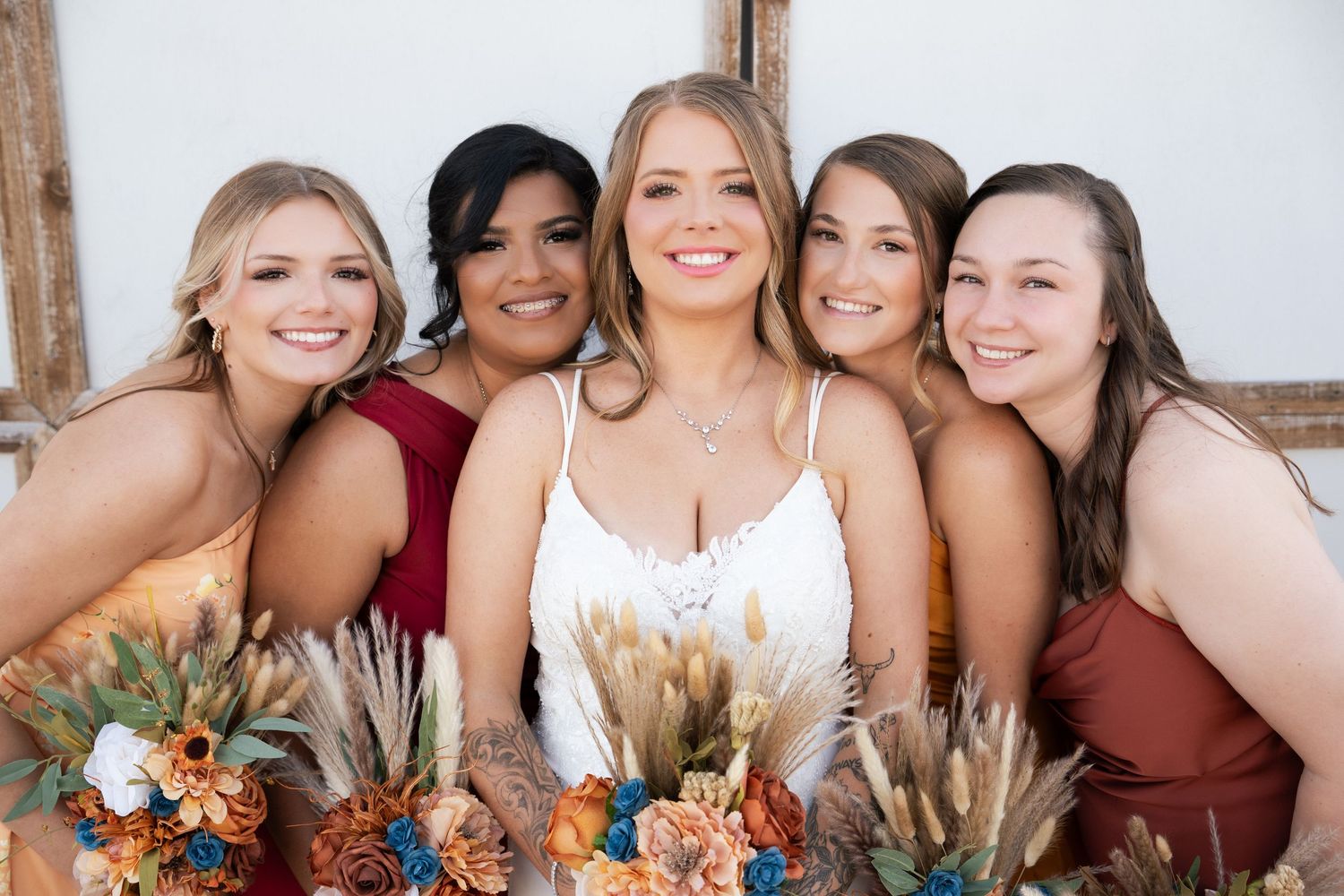 Bride and four bridesmaids smiling closely together holding colorful rustic floral bouquets.
