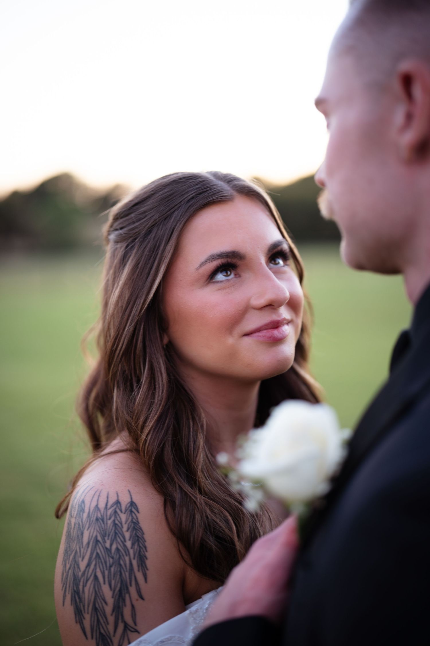 Tattooed bride with long brown hair smiling up at groom during golden hour.