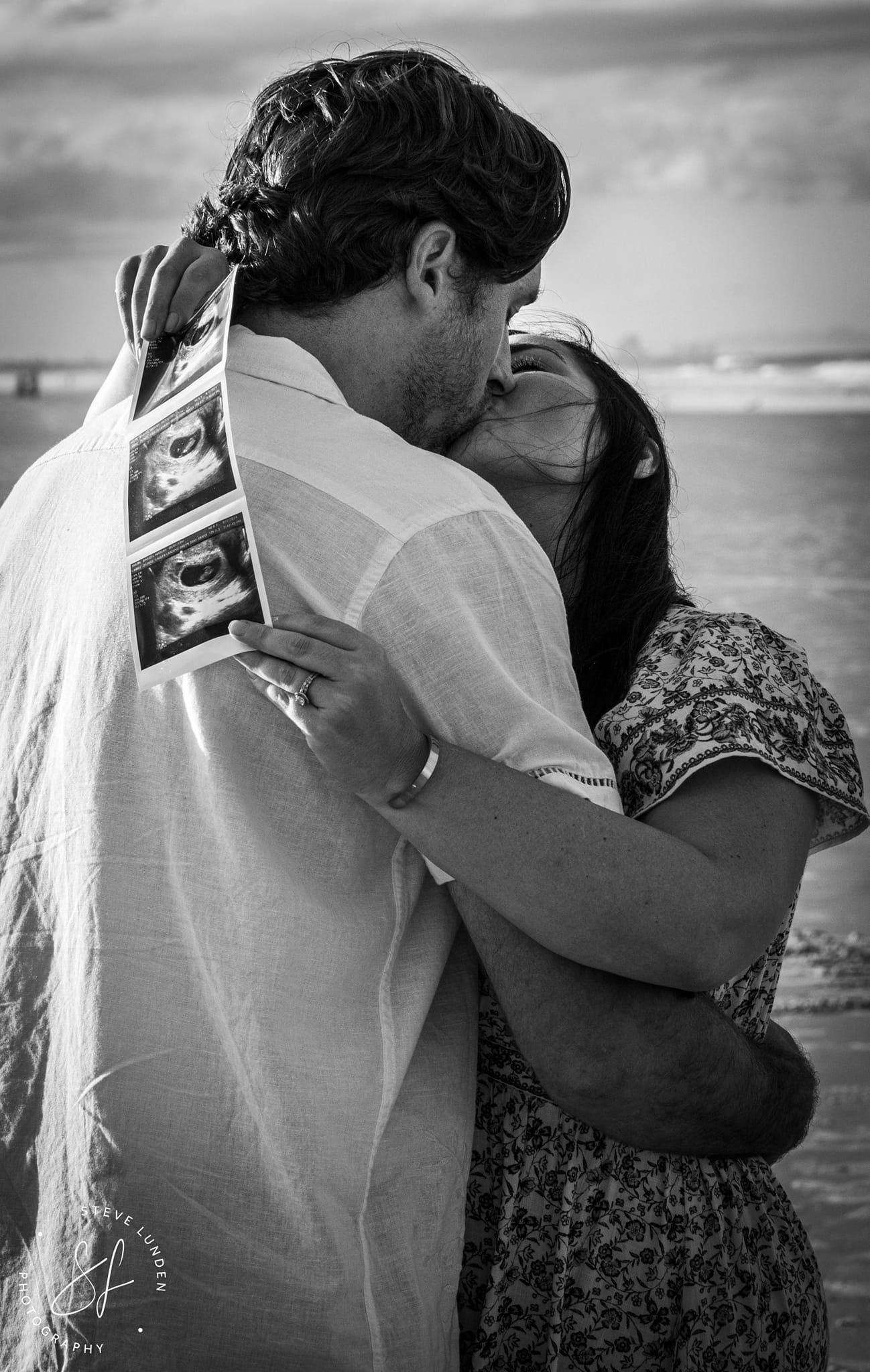young couple kissing while holding ultrasound photos