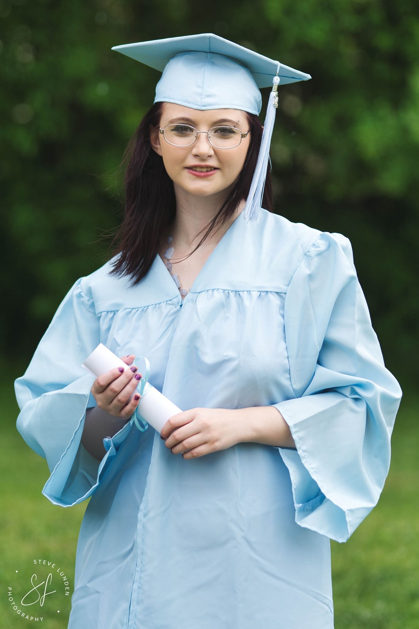 high school graduate posing in cap and gown holding diploma
