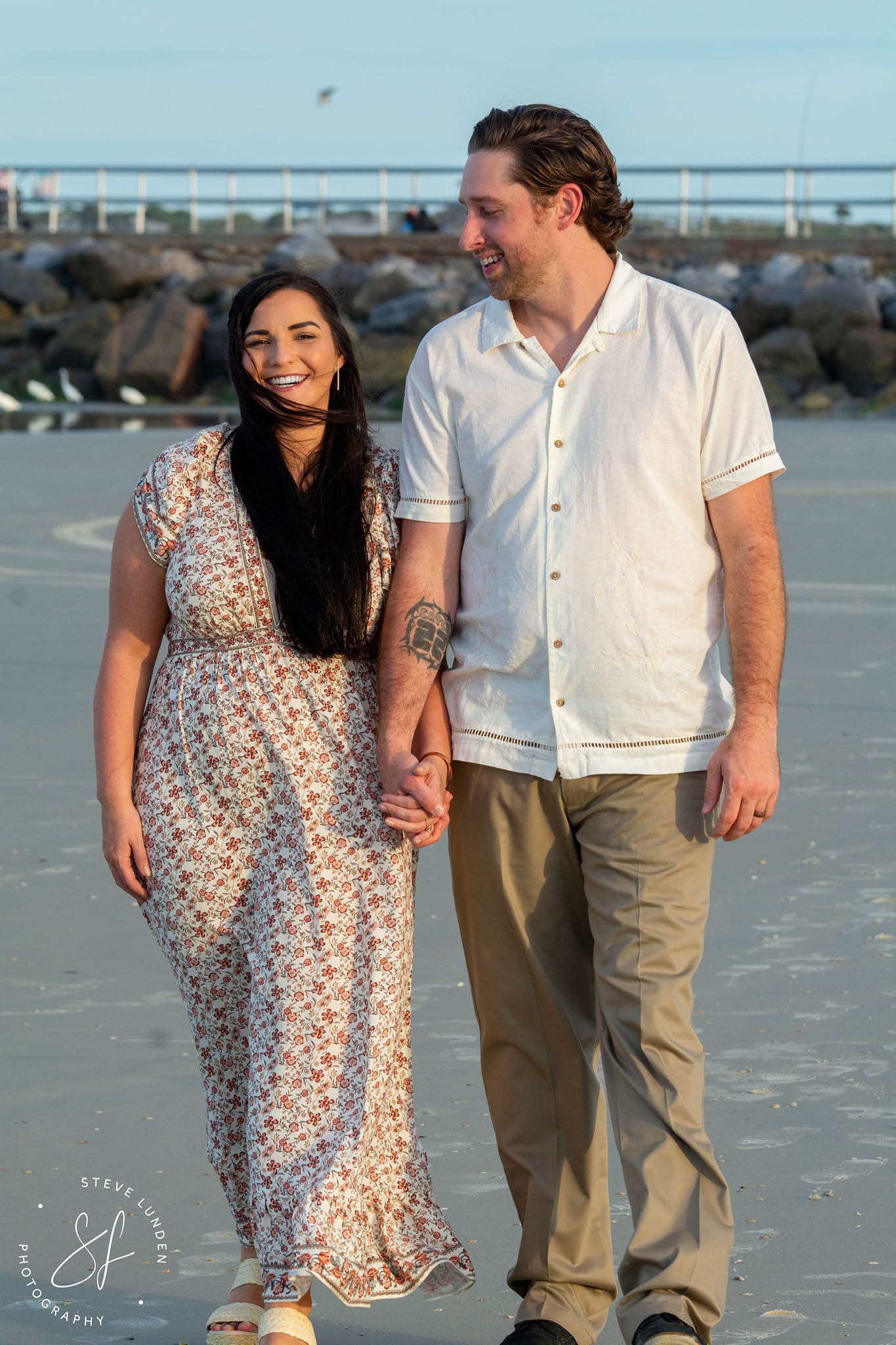 young couple walking on beach in front of jetty