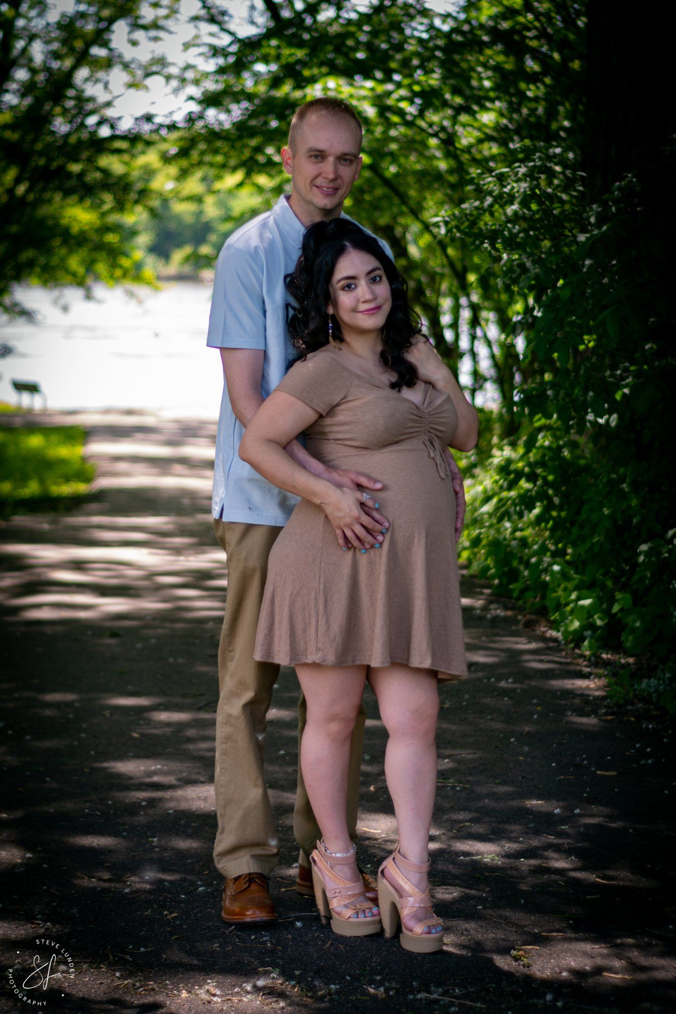 young couple posing near lake, woman is pregnant