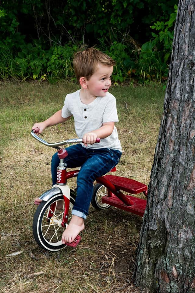 toddler riding a tricycle near a tree