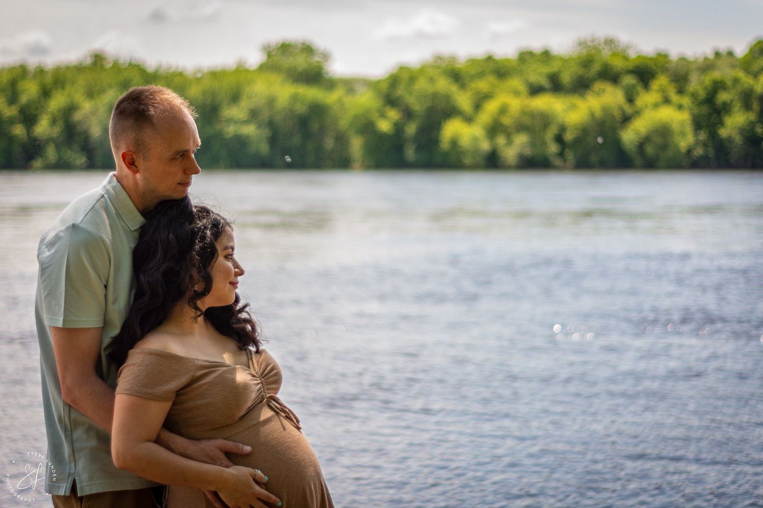 young couple embracing with pregnant woman near lake