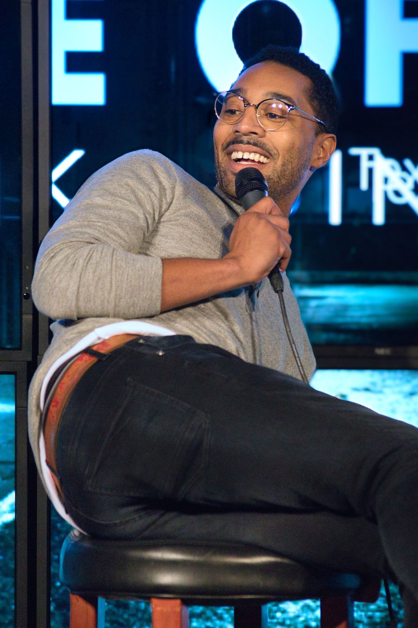 male comedian laying on a stool