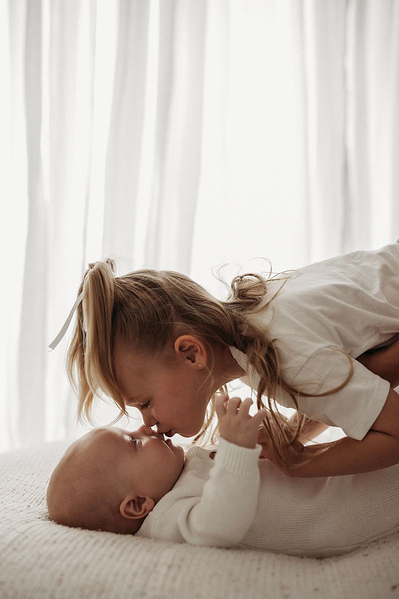 Big sister kissing her baby brother in a timeless sibling portrait at Lou-Lou Pictures in Armstrong Creek.