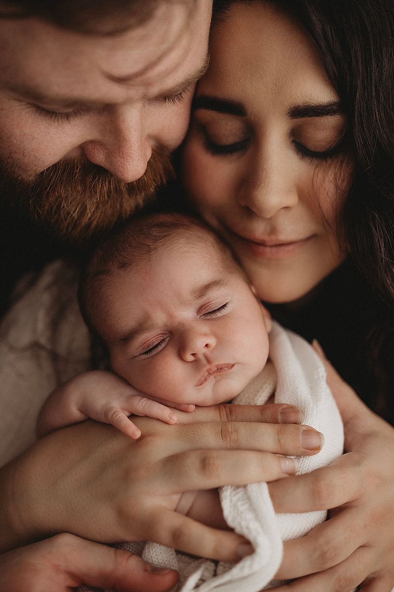 newborn baby girl sleeping in her parents arms during newborn photoshoot in geelong