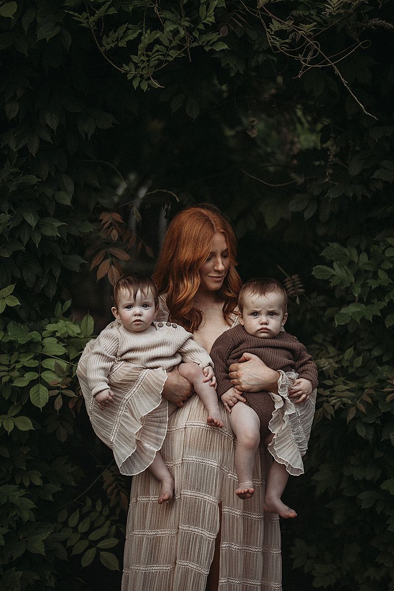 Mother gently cradling her twin babies during a relaxed motherhood photography session, capturing warmth and connection