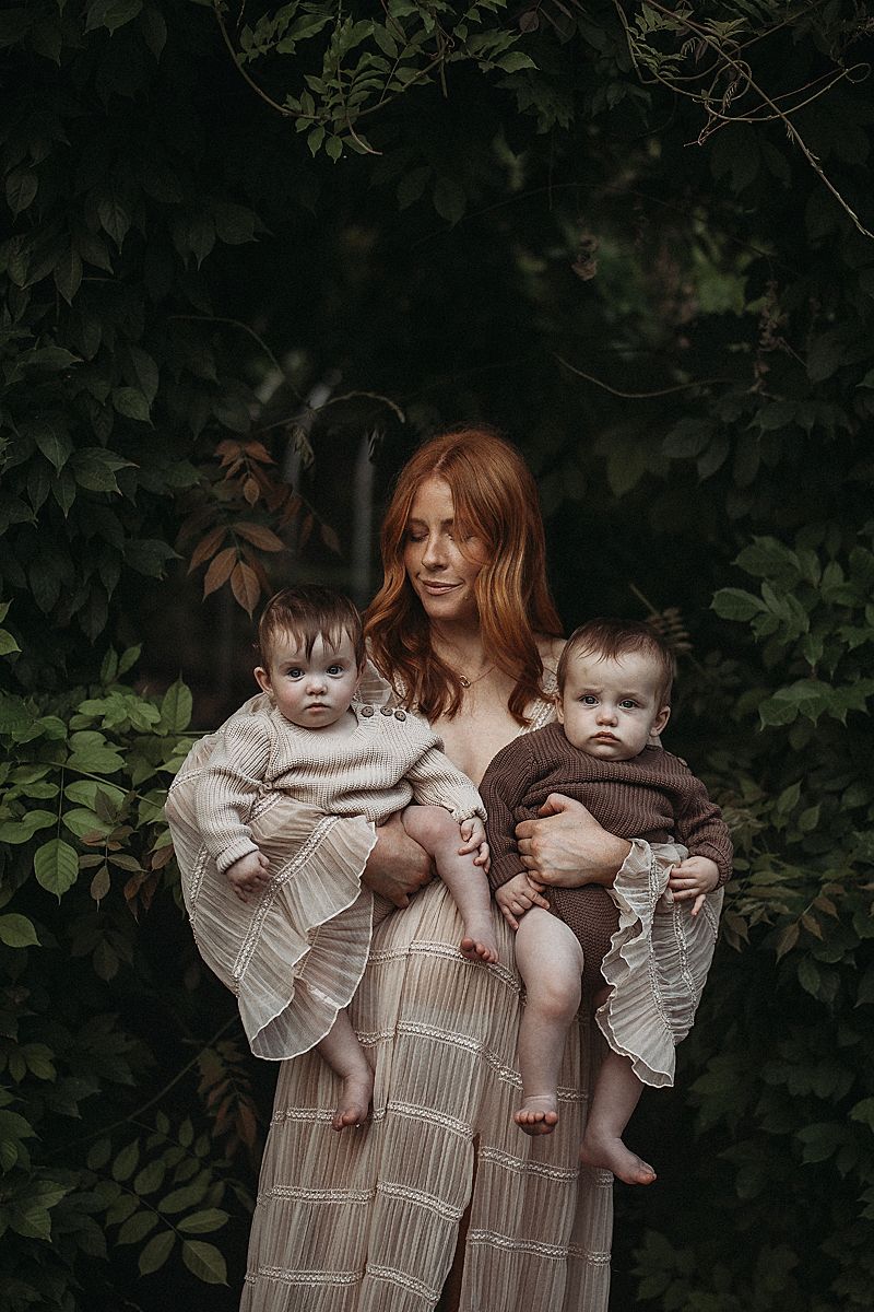 Mother holding her twin babies close during a calm motherhood photography session, captured in soft natural light