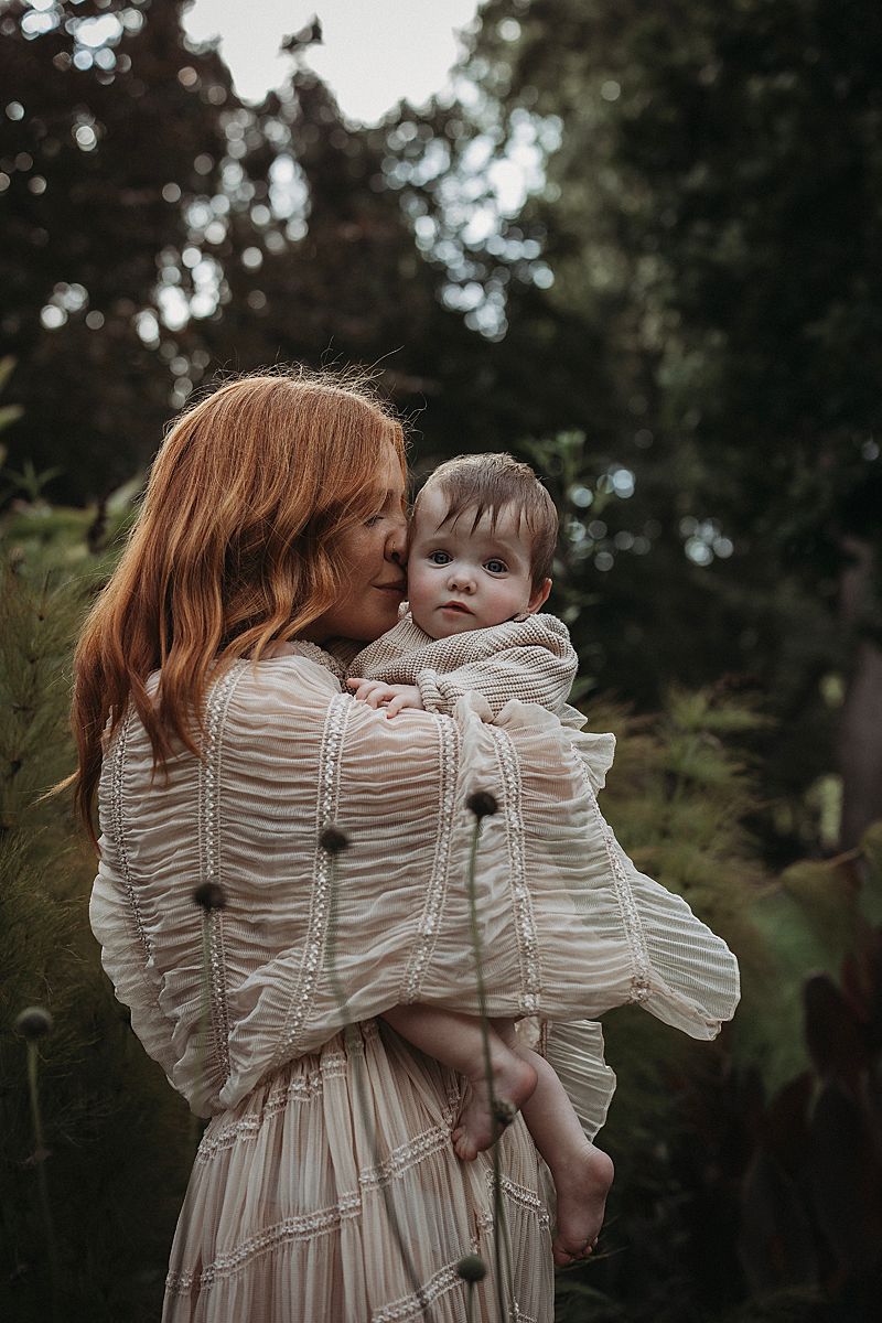 Detail-focused image of a mother’s arms wrapped around her twins, expressing love, safety, and belonging