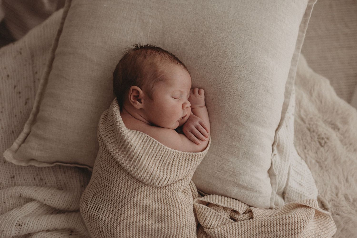 Sleeping newborn in beige blanket, cuddled up for a newborn photography session in Geelong