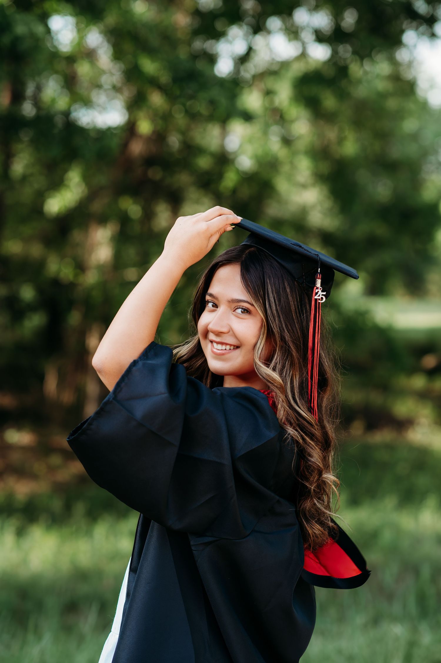 Graduate in black cap and gown poses playfully outdoors during photo session.