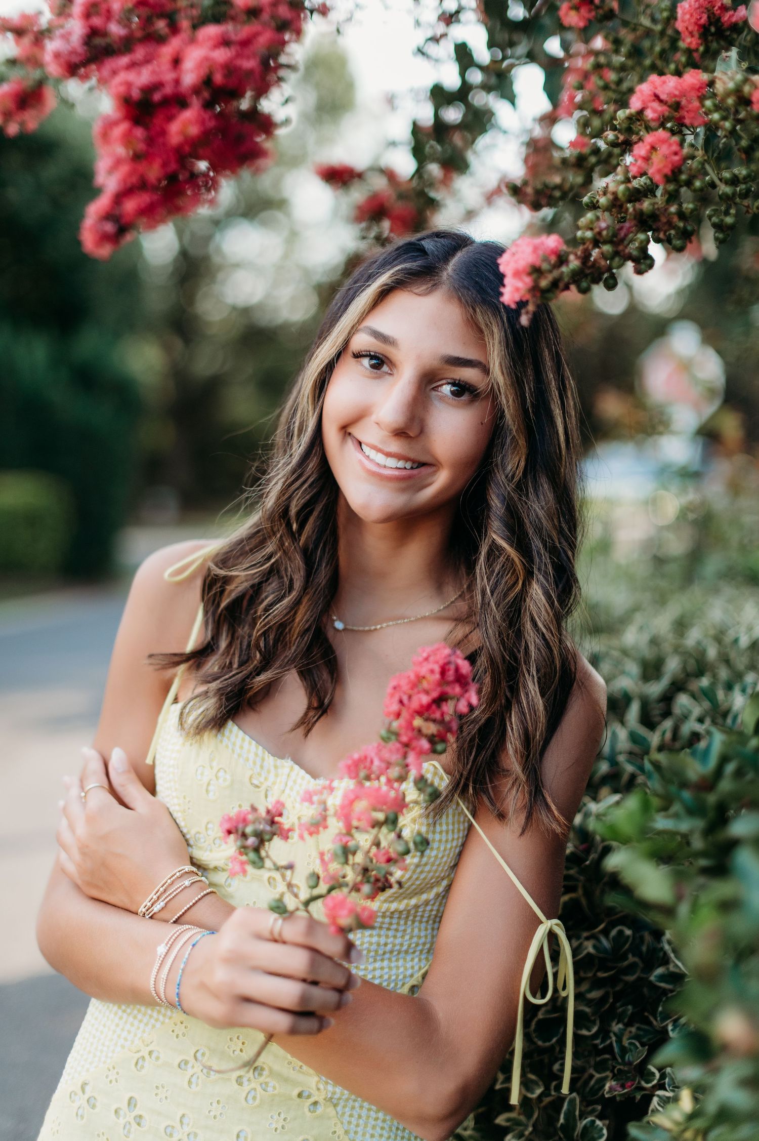 Summer portrait in yellow dress beside blooming pink flowers.