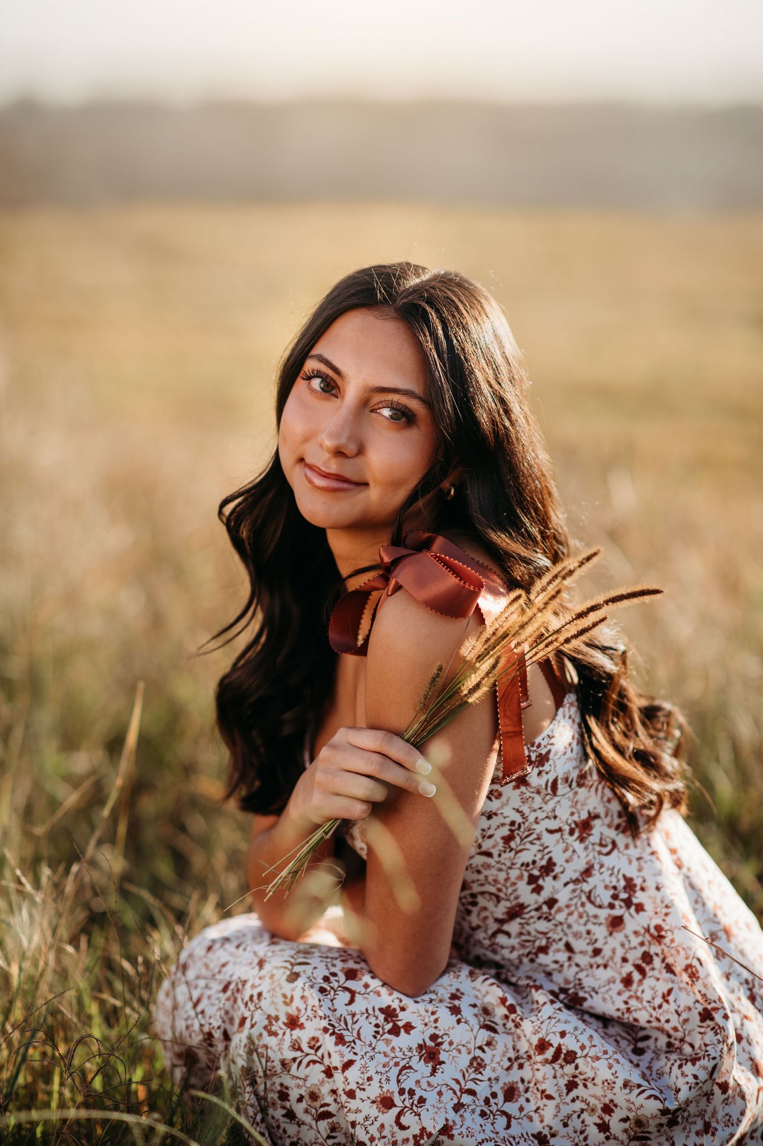 Person in floral dress poses gracefully in golden sunlit field during sunset photoshoot.