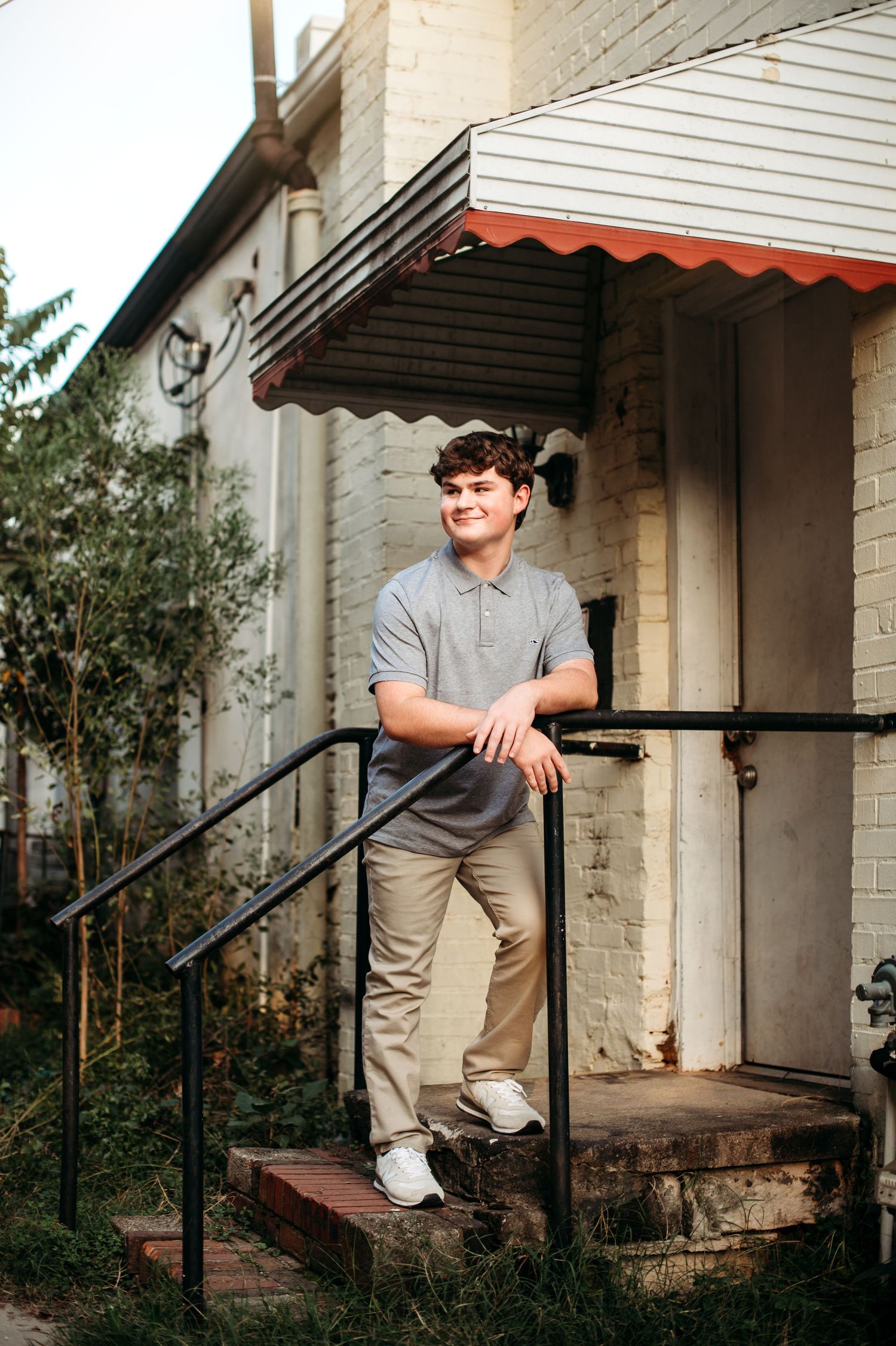 Relaxed outdoor portrait on brick steps with striped awning overhead.