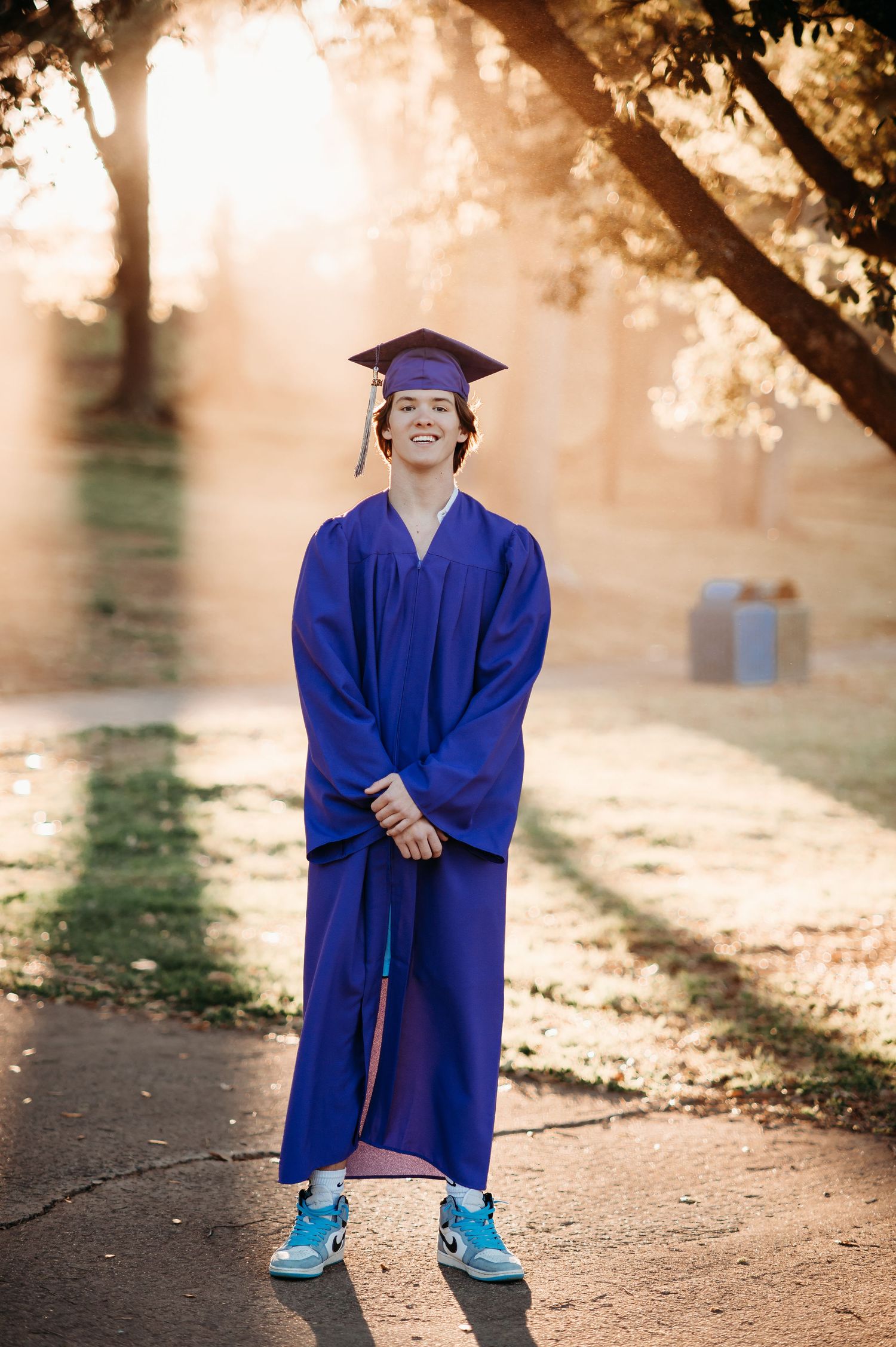 Young student in blue graduation gown poses joyfully outdoors.