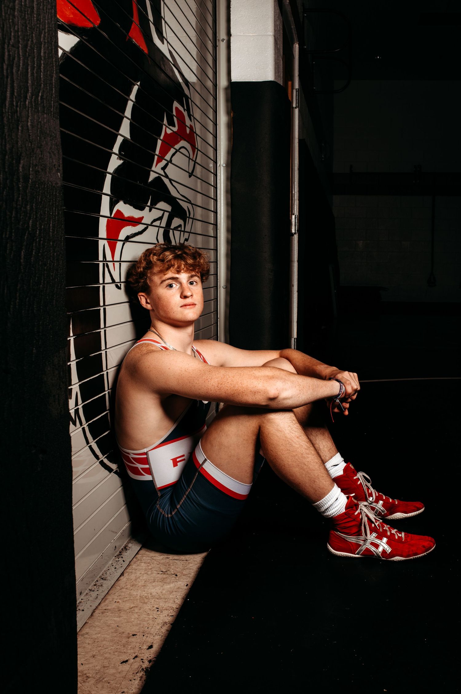 Dramatic low light portrait series against dark wall featuring red athletic shoes and moody shadows.