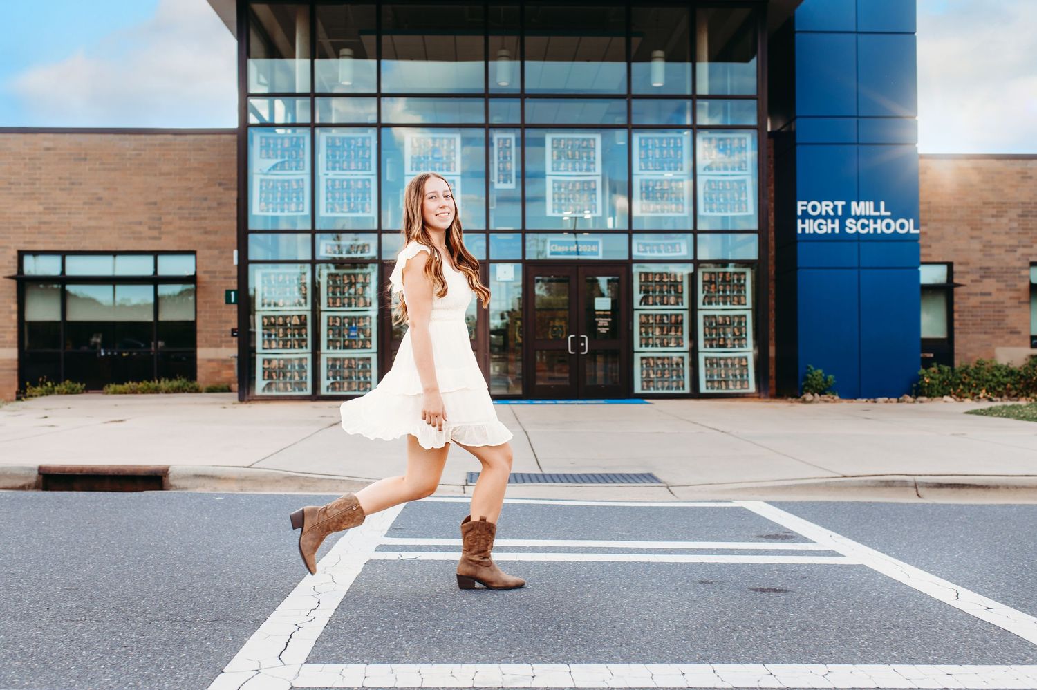 Person in white dress and boots poses playfully in front of school entrance.