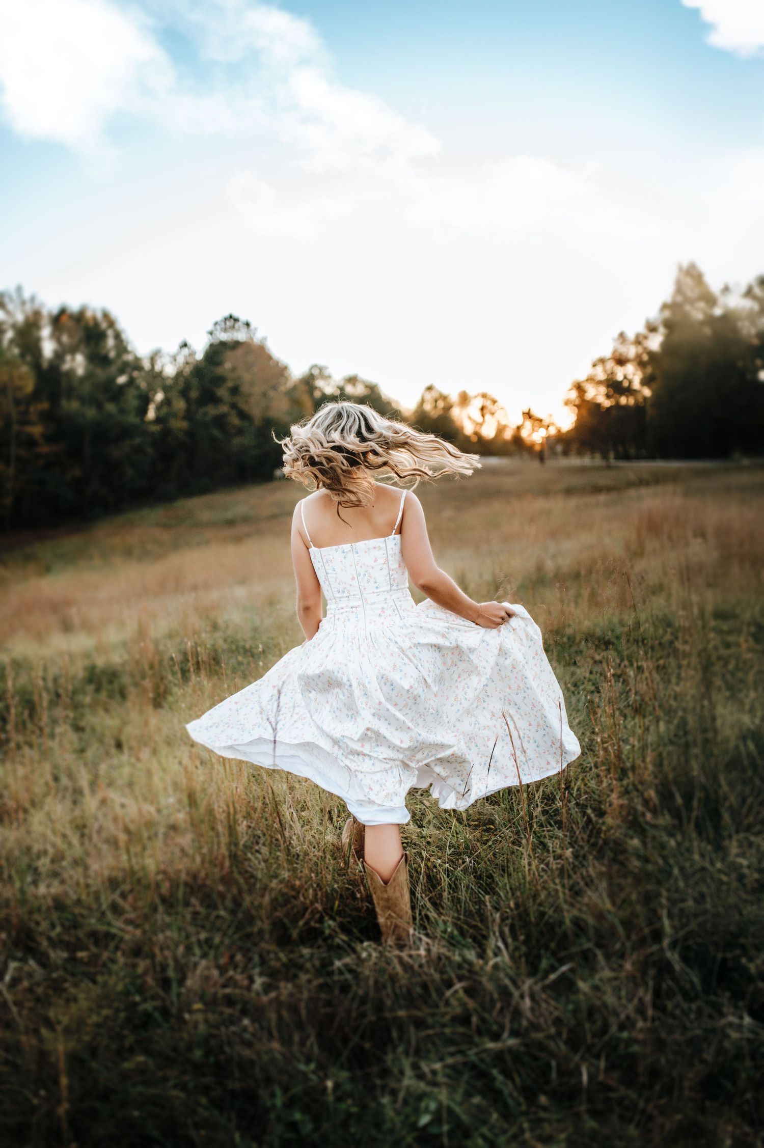 A white dress twirls gracefully in a golden meadow at sunset creating an ethereal silhouette against the landscape.
