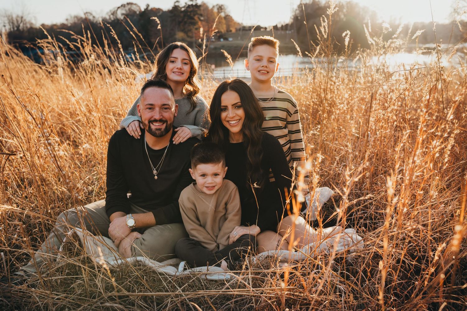 Group sits together in golden autumn field during sunset photoshoot with tall grass surrounding them.