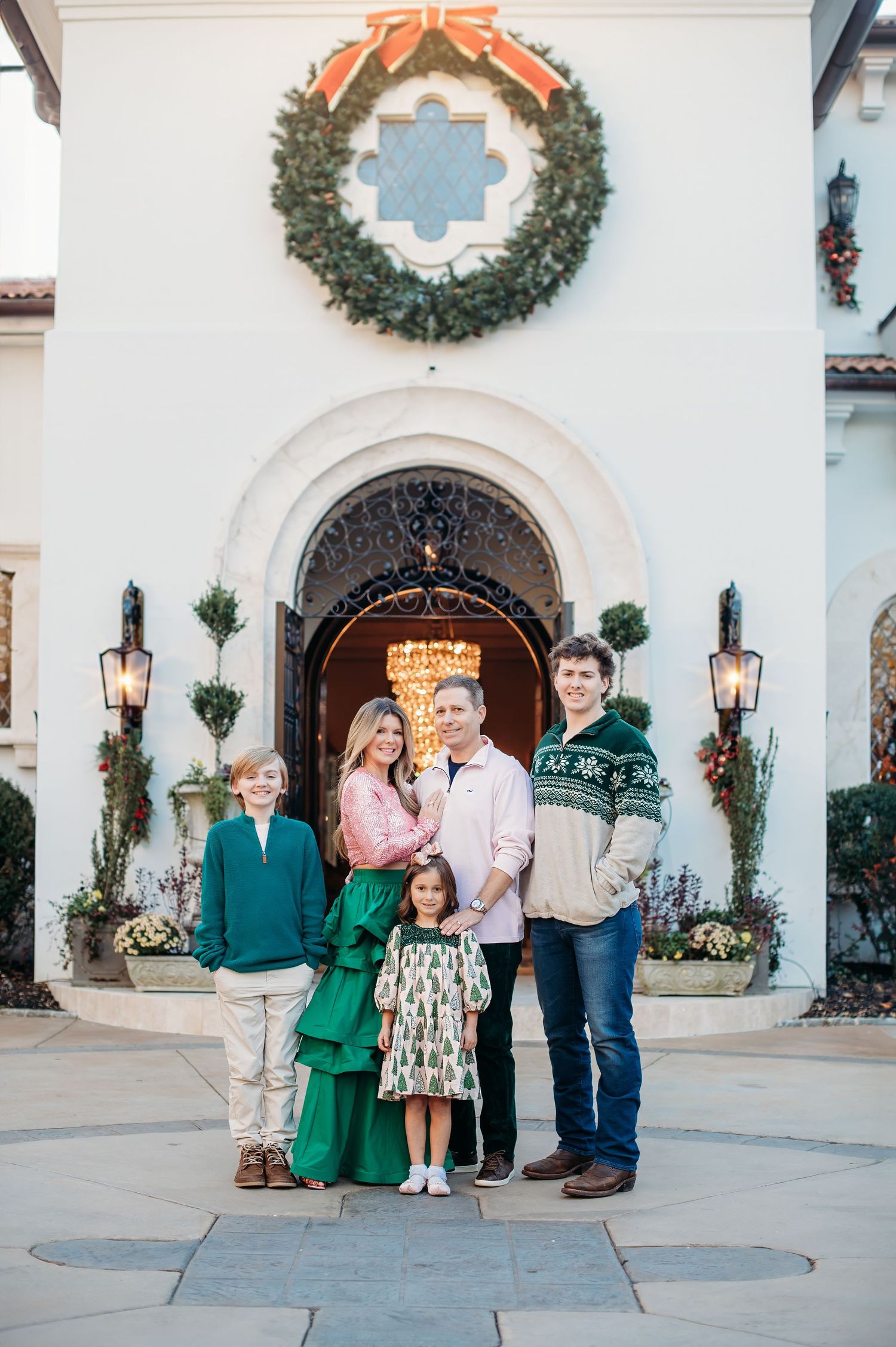 Family stands in front of Spanish colonial style doorway decorated with Christmas wreath and lanterns.
