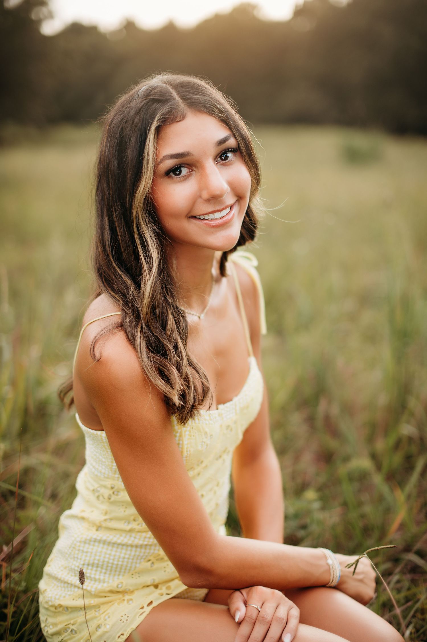 Natural outdoor portrait in yellow sundress sitting in sunlit field.