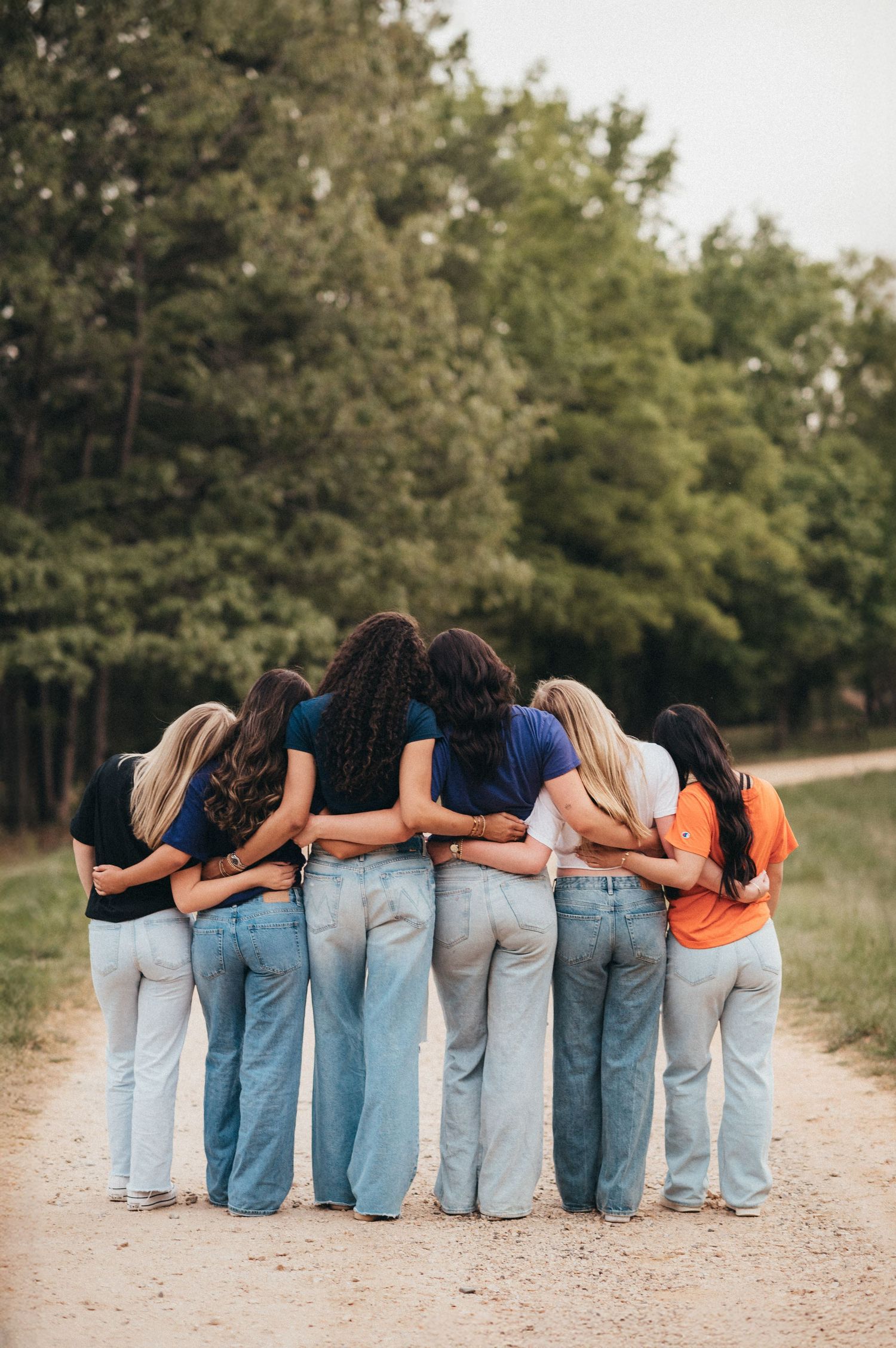 Group photo showing row of friends in jeans posing with their backs to camera on dirt path. fort mill, sc class of 2027