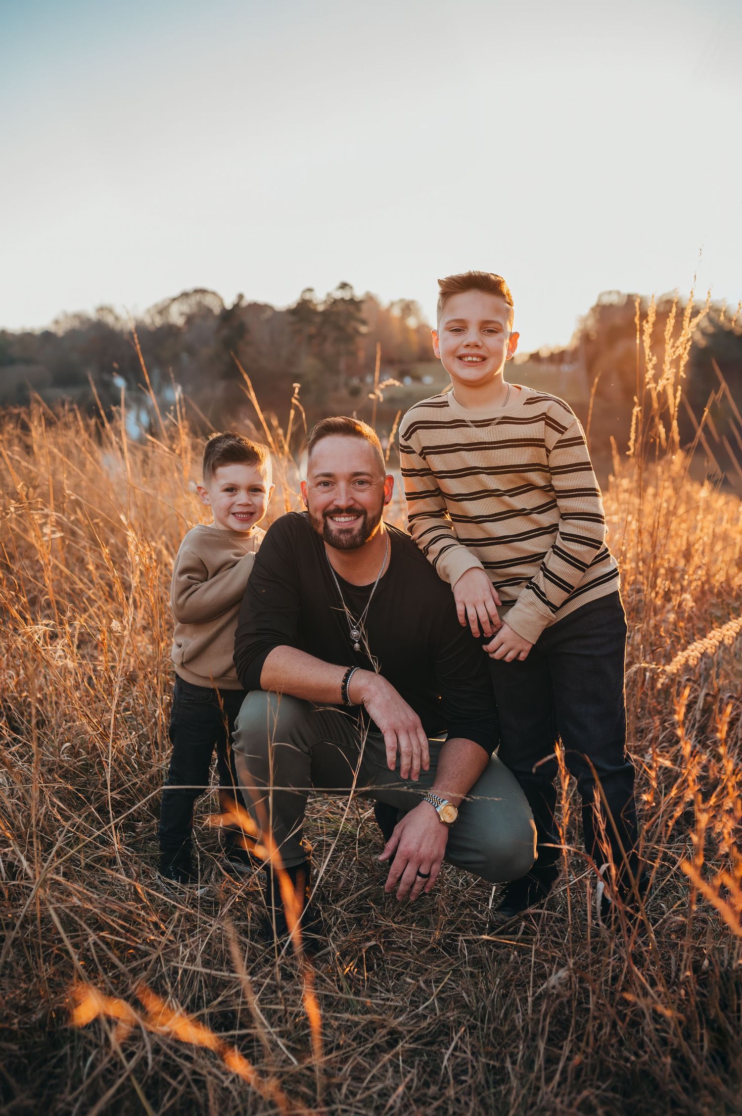 Family enjoying a warm sunset moment together in tall golden grass during an outdoor photo session.