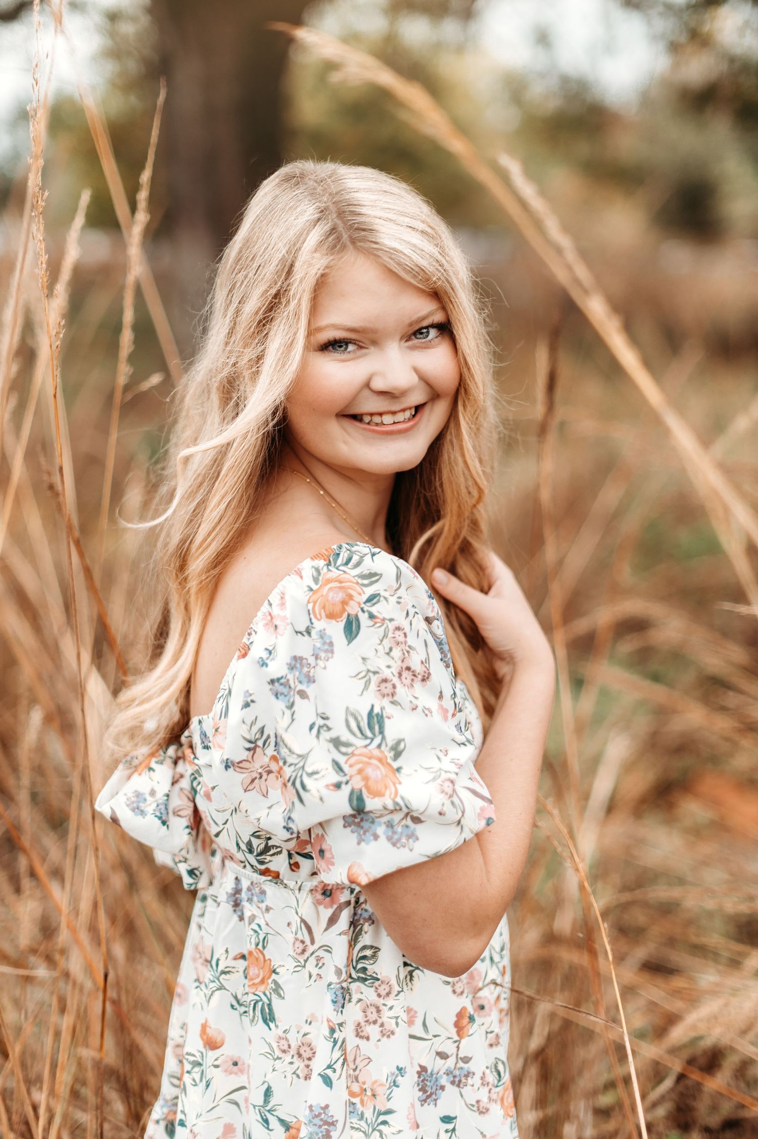 Outdoor portrait in floral dress among tall grass during golden hour.