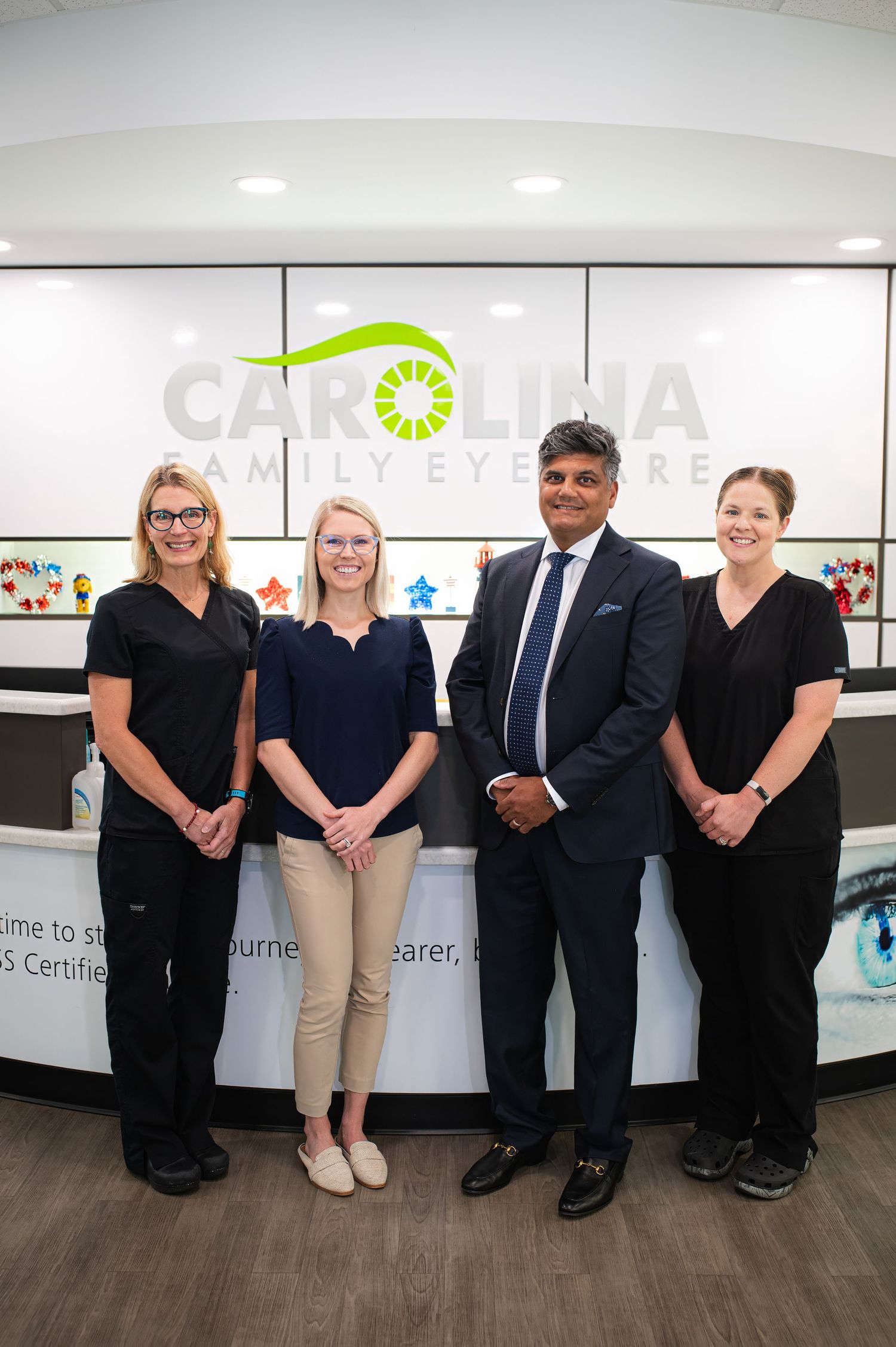 Four professionals stand in front of a branded reception desk with a green and white logo on the wall.