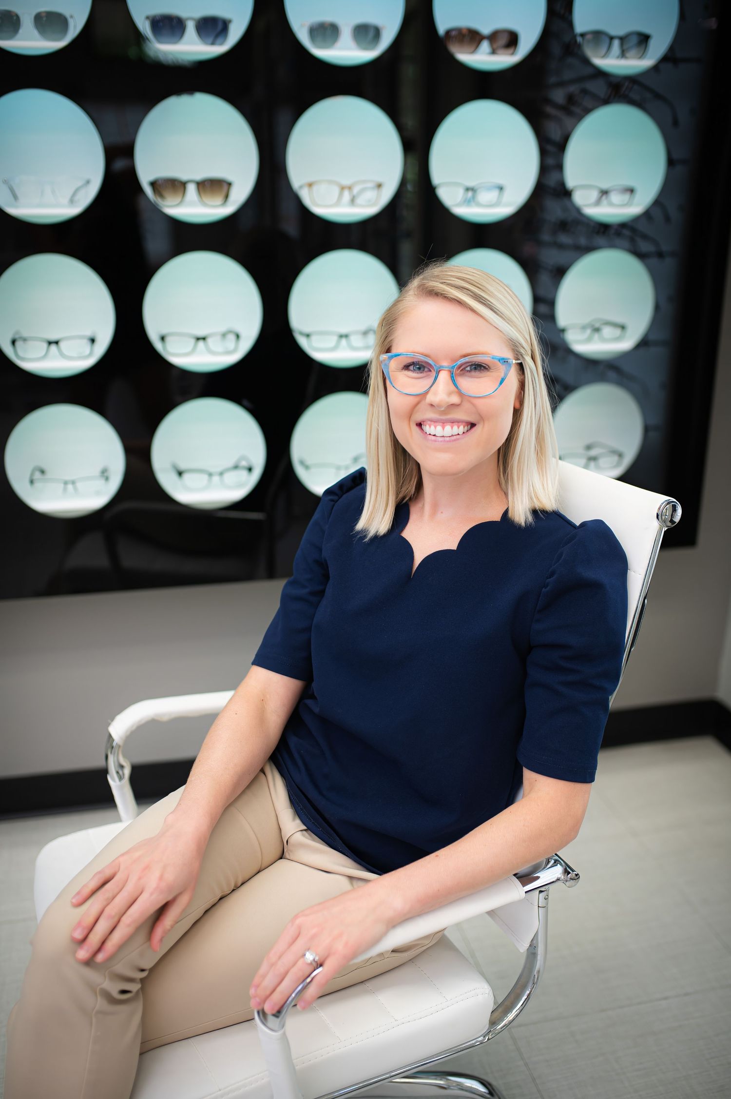 Healthcare professional sits in white chair smiling in office with x-ray displays on wall behind.