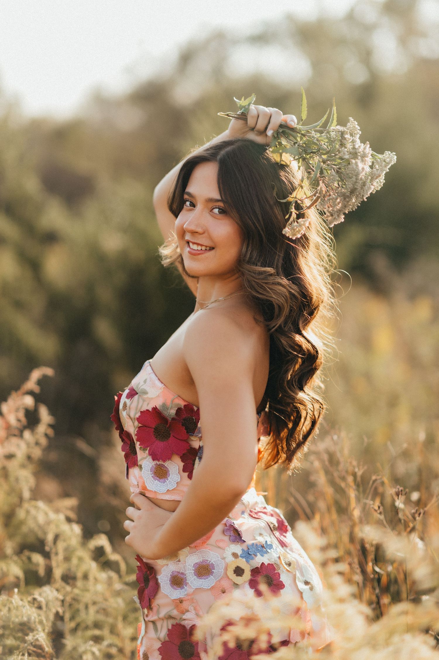 Joyful summer portrait in a floral dress among tall grasses at golden hour.