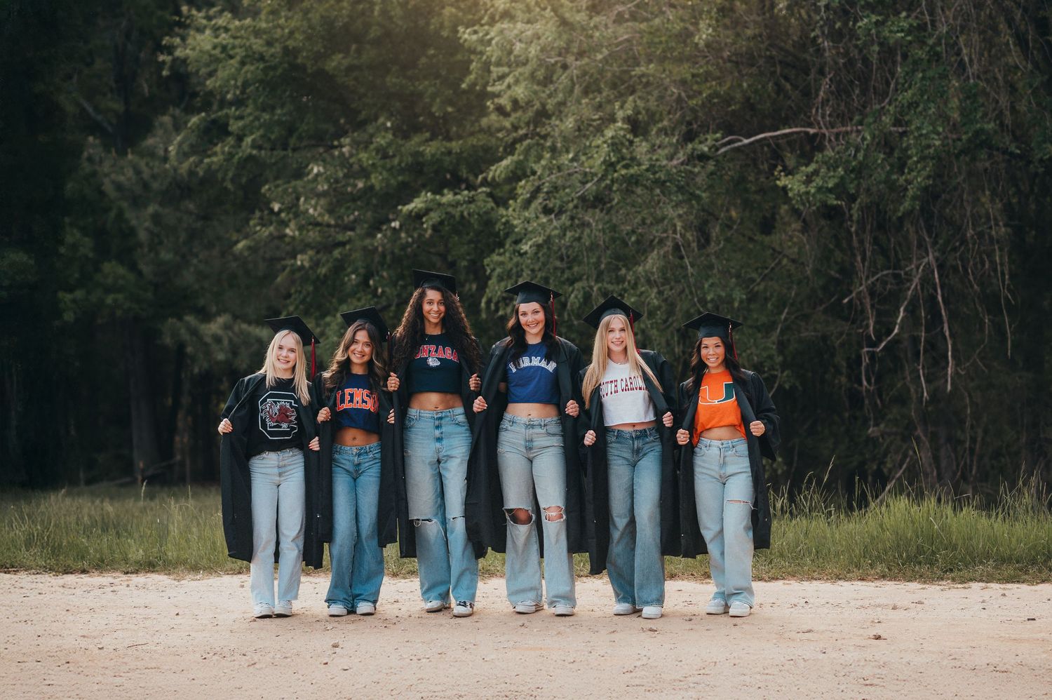 A group of friends in matching denim jeans pose together on a dirt path near a wooded area.