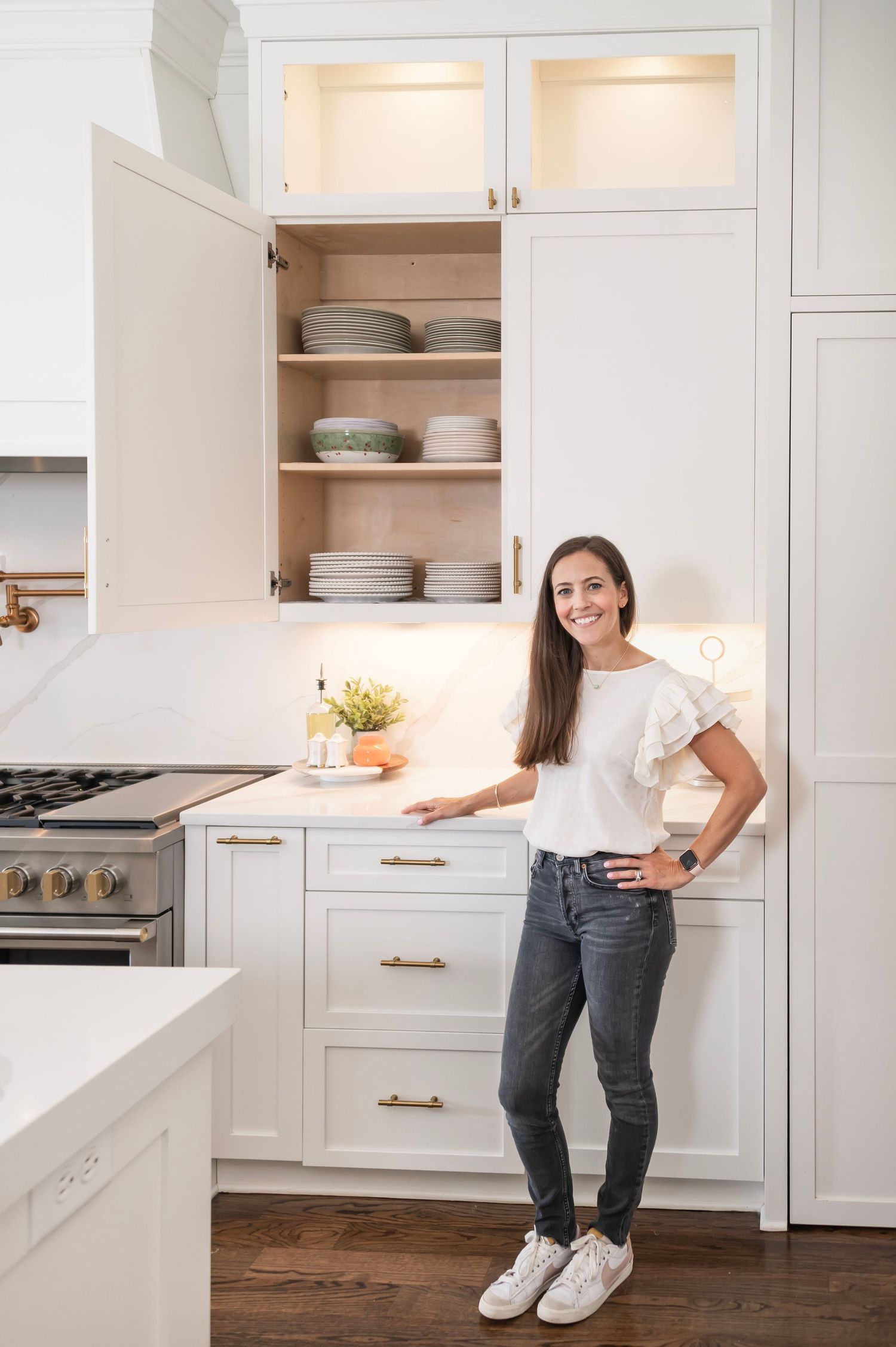 Modern white kitchen interior with illuminated cabinets, quartz countertops and hardwood floors features open cabinet storage.