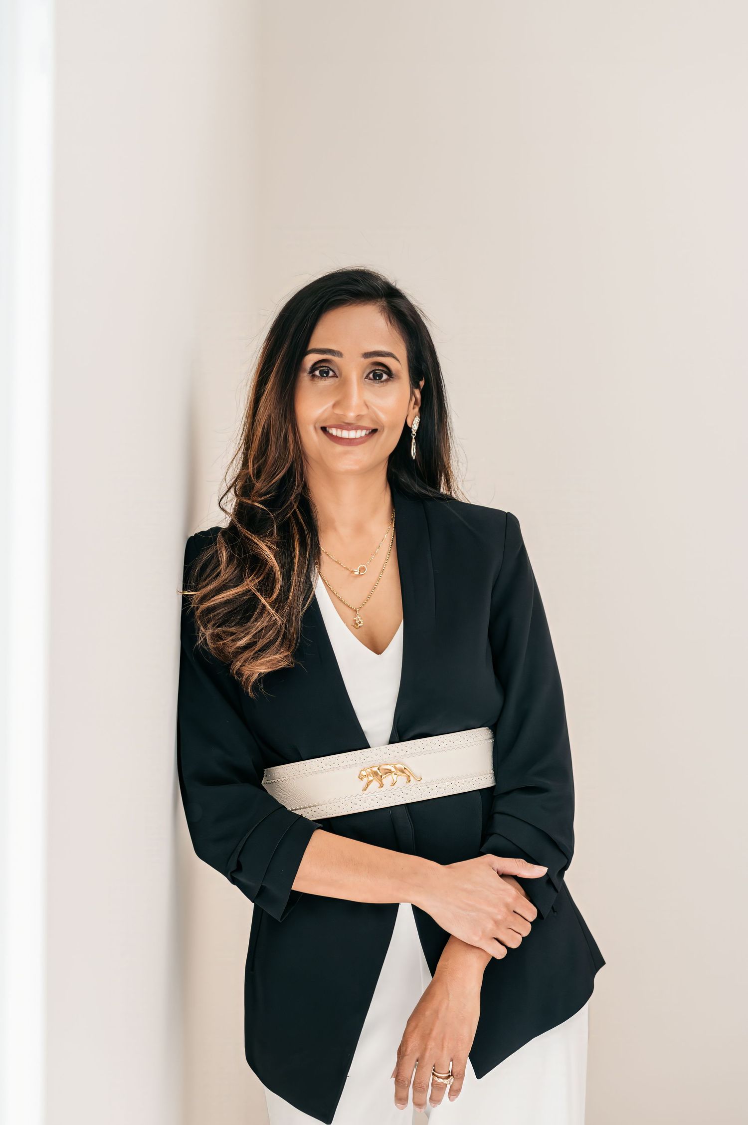 Professional portrait of someone in a black blazer with white accent against light background.