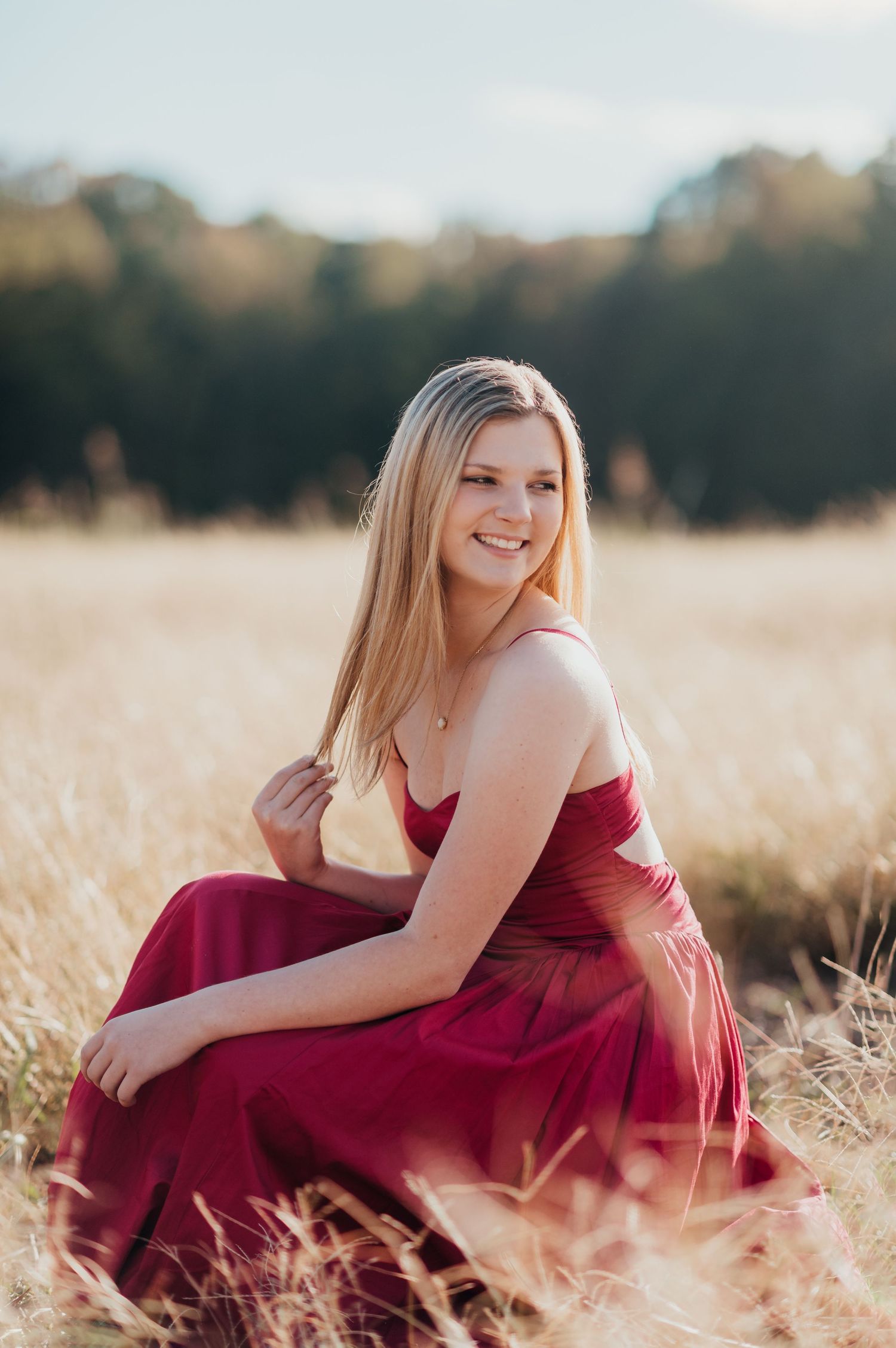 A romantic portrait in a burgundy dress sitting in a golden wheat field at sunset.