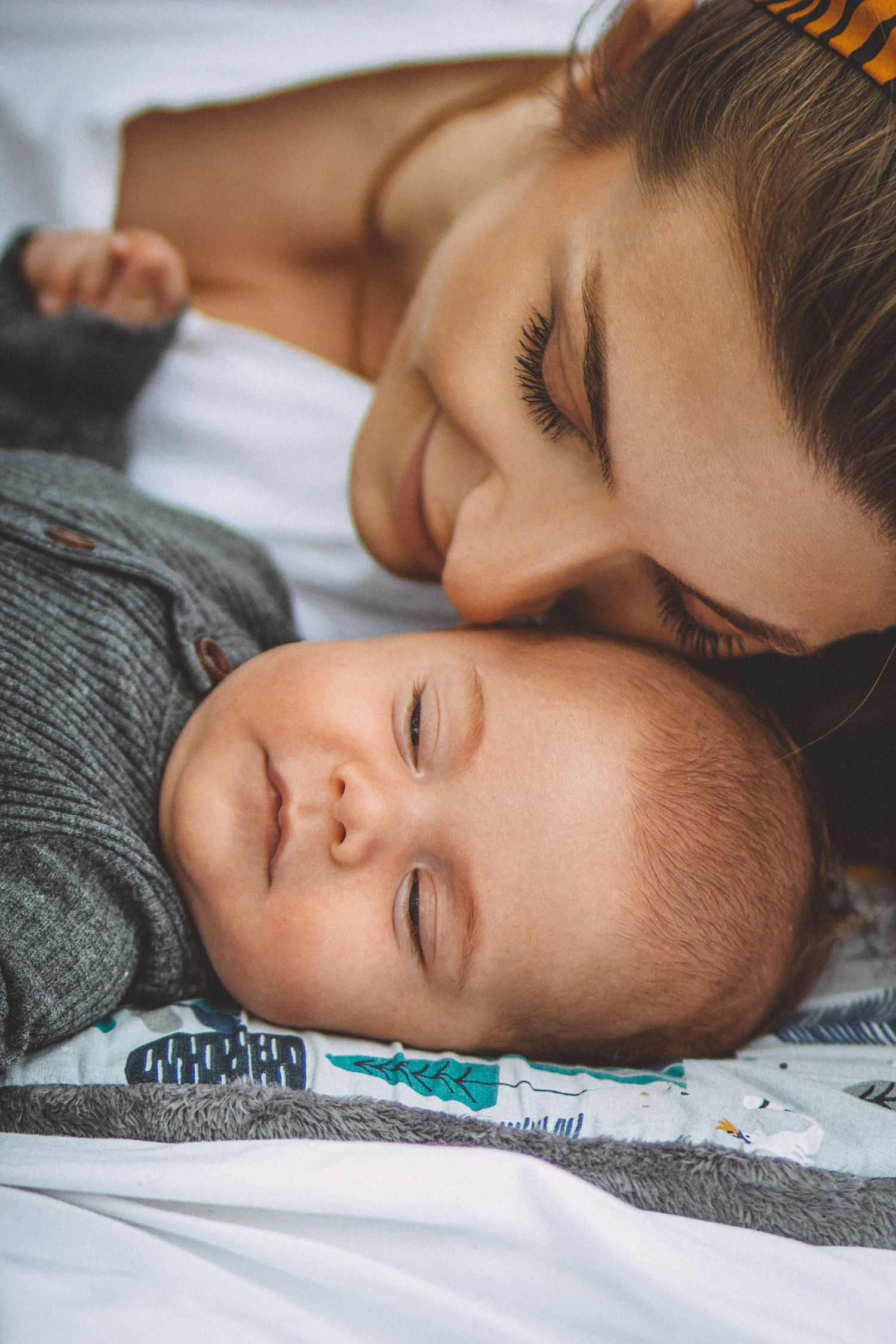 Child sleeping peacefully on gray bedding in natural light.