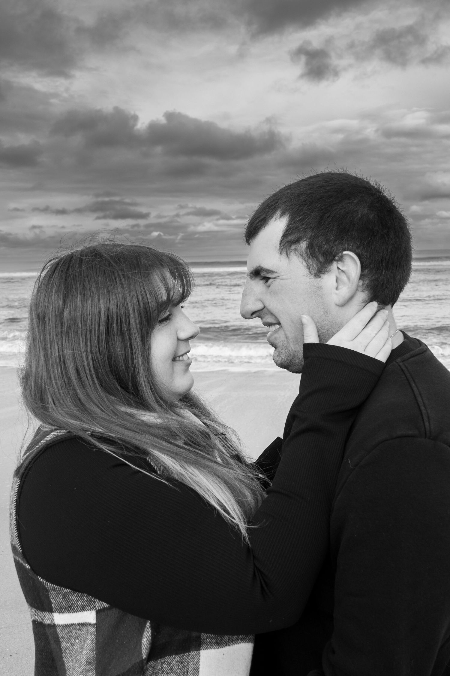 A romantic black and white photo series showing a couple embracing on a cloudy beach.