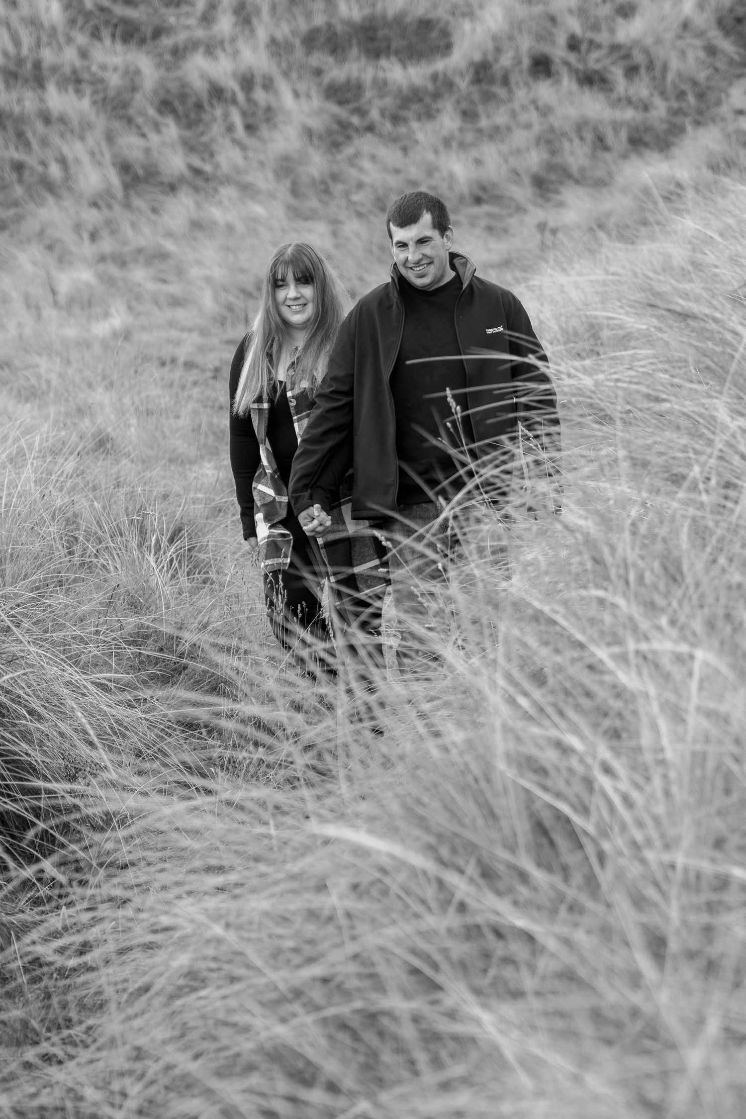 A couple sits together in tall grass field shown in black and white progression across multiple connected photos.
