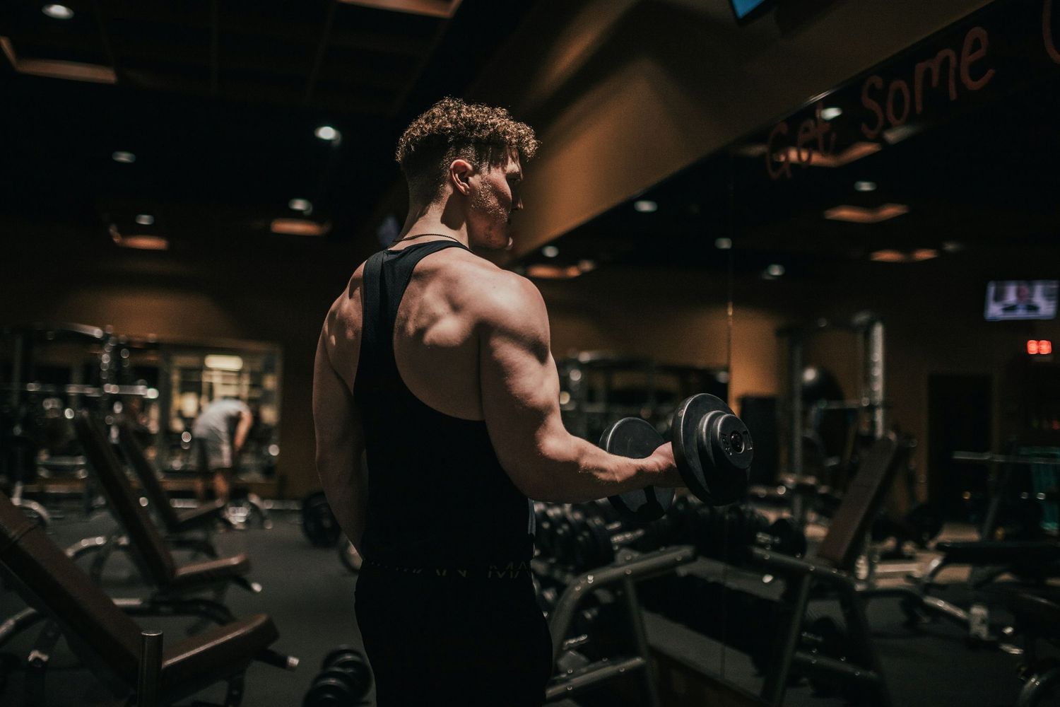 Person working out using resistance bands and weights in a dark modern gym while looking at camera.